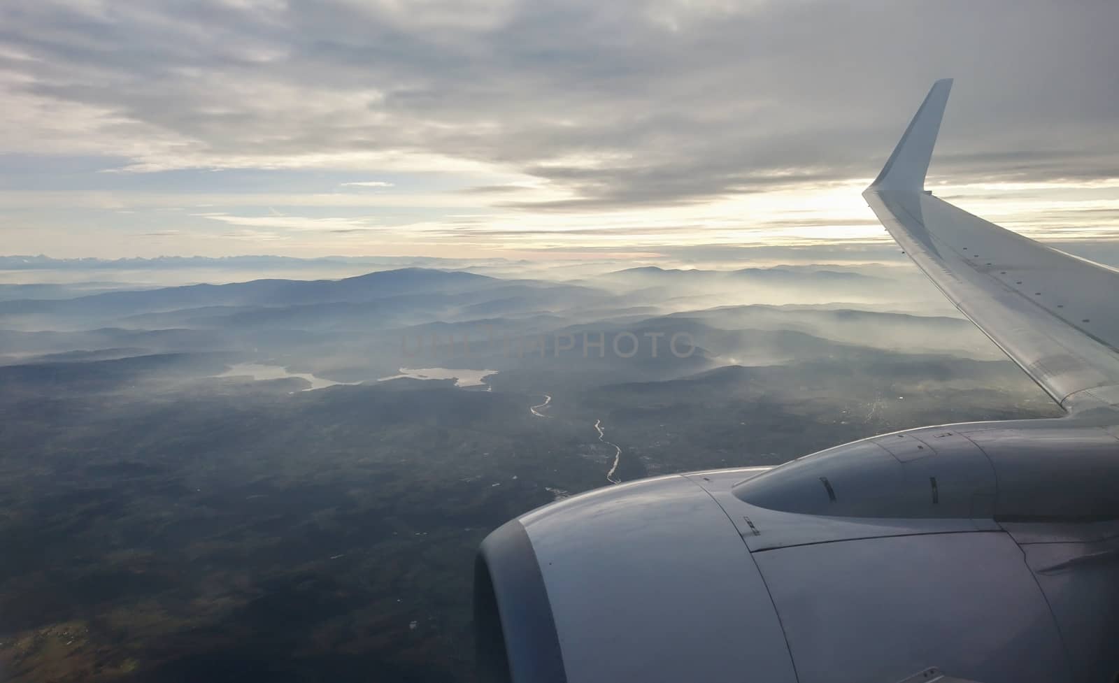 View through window over wing and engine during flight. View of country and mountains from plane during landing.