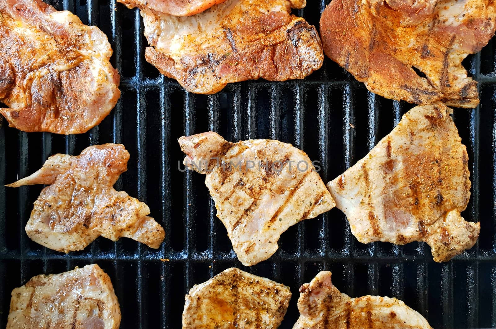 Top view of pork and chicken marinated slices on grill during BBQ grilling.