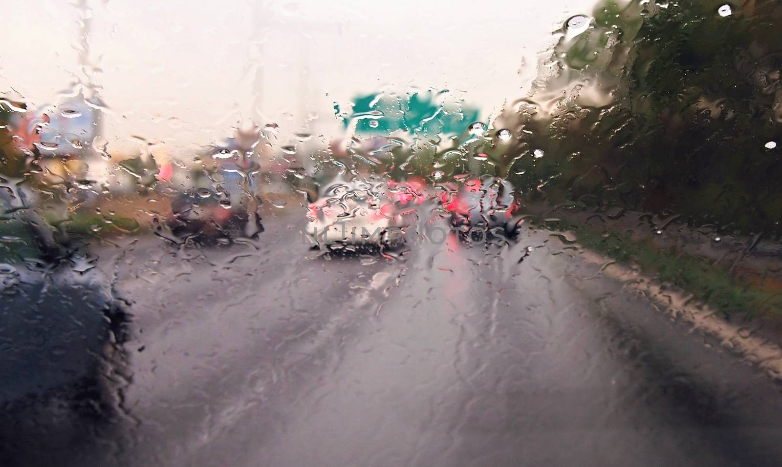 Driving a car in the rain and storm in heavy traffic. View through a windshield with rain drops during driving a car. Shallow depth of field.