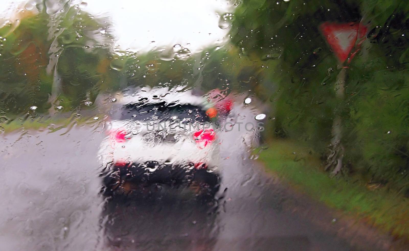 Driving a car in the rain and storm in heavy traffic. View through a windshield with rain drops during driving a car. Shallow depth of field.