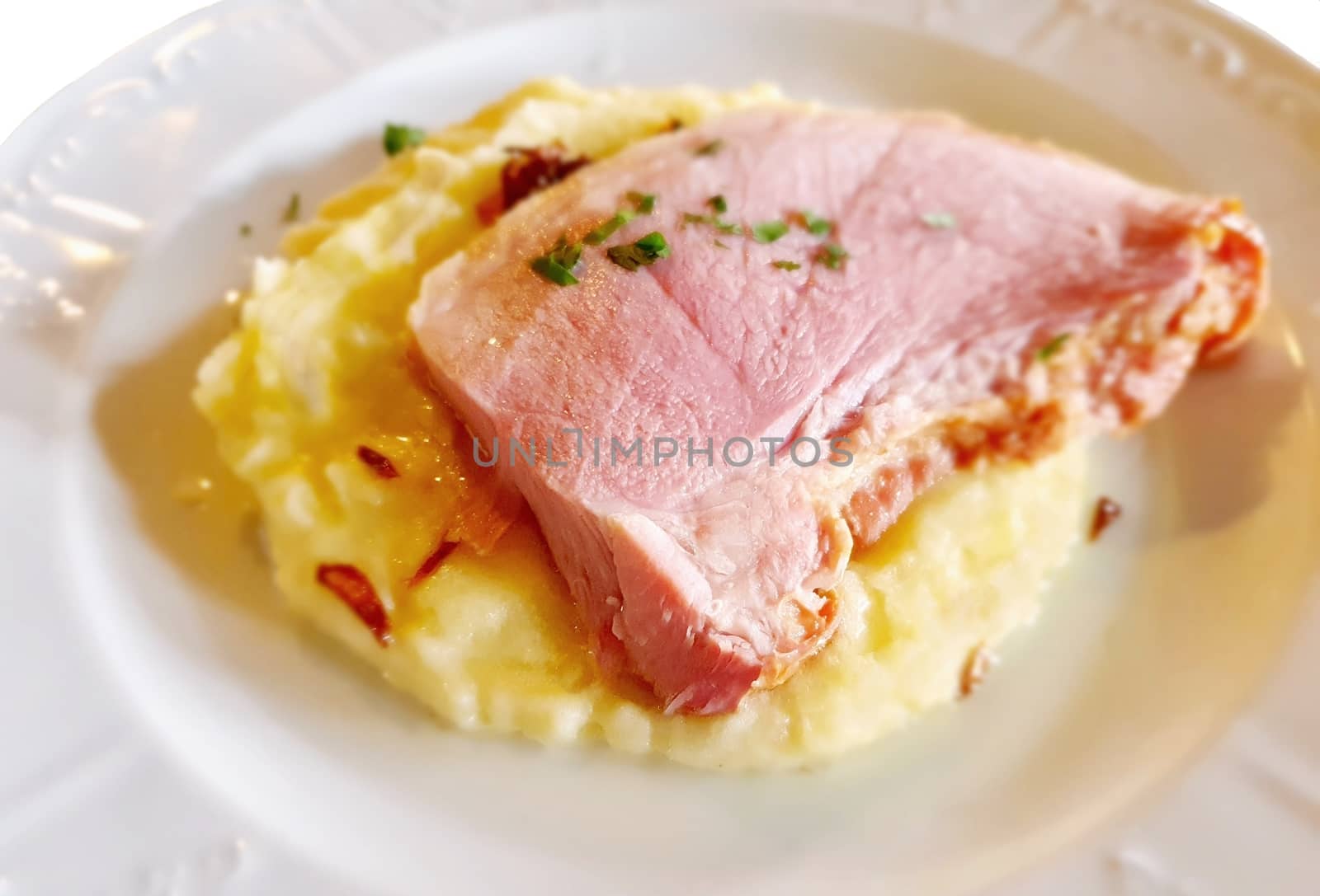 Roast ham slice with mashed potatoes on white plate.