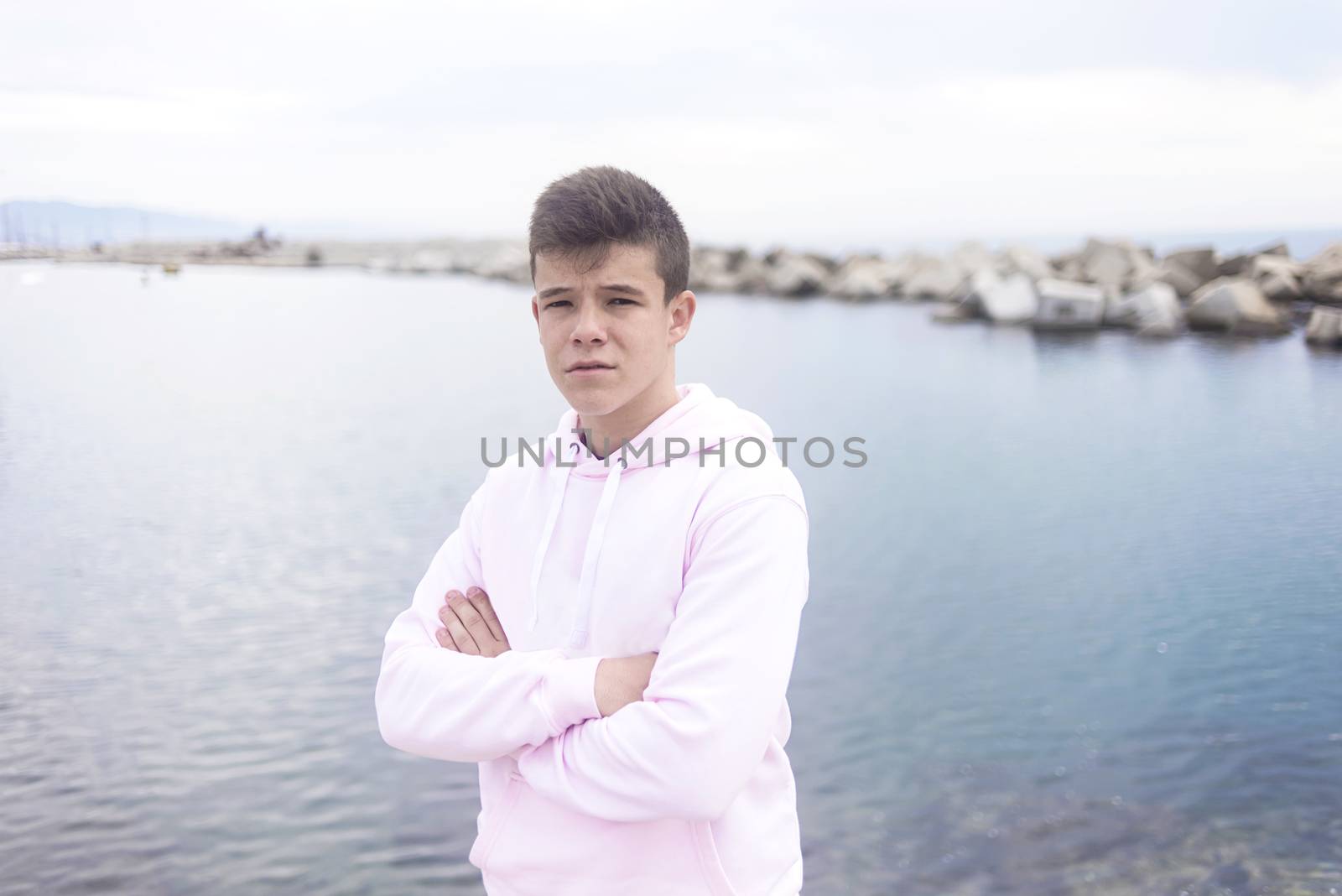 Young teenager with crossing arms standing on promenade while looking at camera