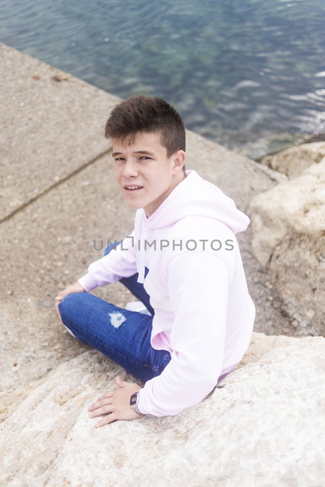 Young teenager male sitting on breakwaters while looking at camera