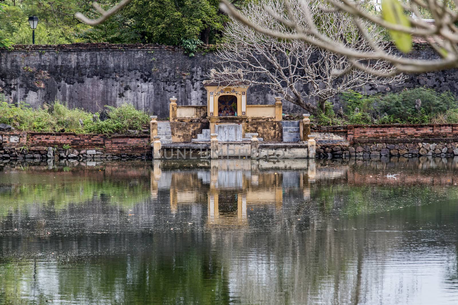 Hue, old capital of Vietnam from 1802 to 1945. Shrine at waters edge reflected in lake. Architecture and details of buildings. A major attraction is its vast, 19th-century Dai Noi Citadel, surrounded by a moat and thick stone walls. It encompasses the Imperial City, with palaces and shrines. High quality photo