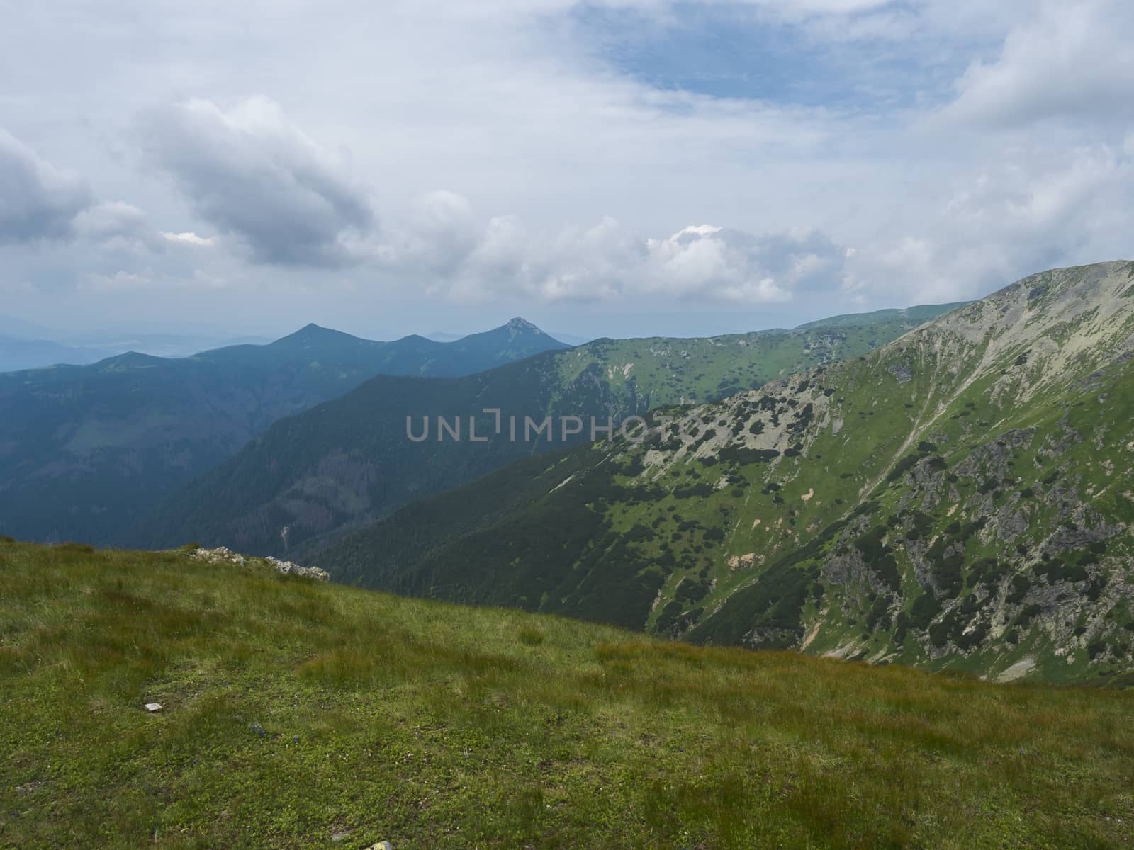 Beautiful mountain landscape with lush green grass, meadow and bare mountain peaks on ridge Western Tatras mountains, Rohace Slovakia, summer dramatic clouds sky background.