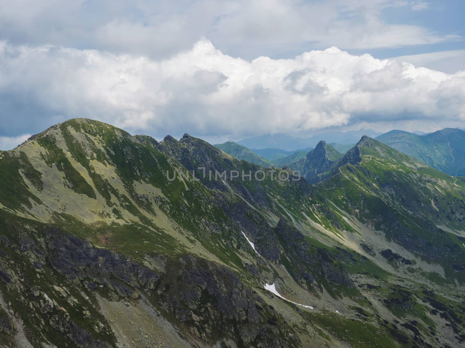 View from Banikov peak on Western Tatra mountains or Rohace panorama. Sharp green mountains - ostry rohac, placlive and volovec with hiking trail on ridge. Summer blue sky white clouds
