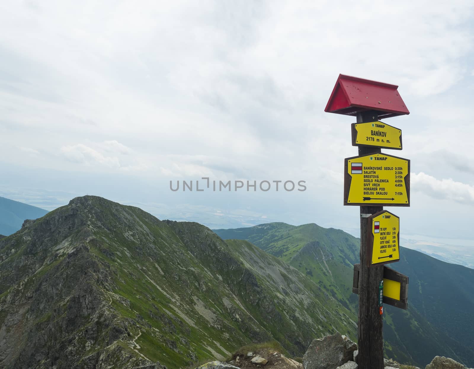 Trail signpost at Top of the peak Banikov at Western Tatra mountains or Rohace. Sharp green mountains with hiking trail on ridge. Summer blue sky white clouds
