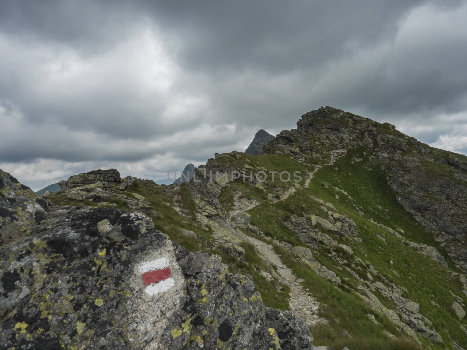 red trail post sign at steep hiking path on ridge of rohace mountain to peak ostry rohac. Sharp green rocks, .Summer blue sky white clouds, Slovakia, Western Tatra mountain