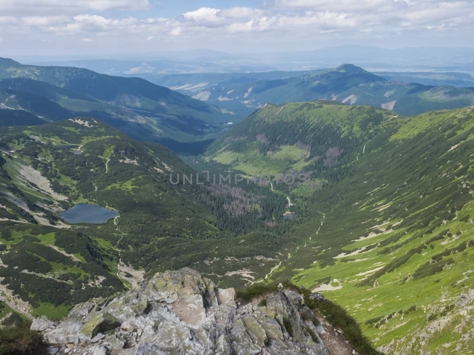 Beautiful vivid blue mountain lake Rohacske pleso with green mountain peaks and hiking path. view from the Ostry rohac, Western Tatras mountains, Rohace Slovakia, summer sunny day blue sky.
