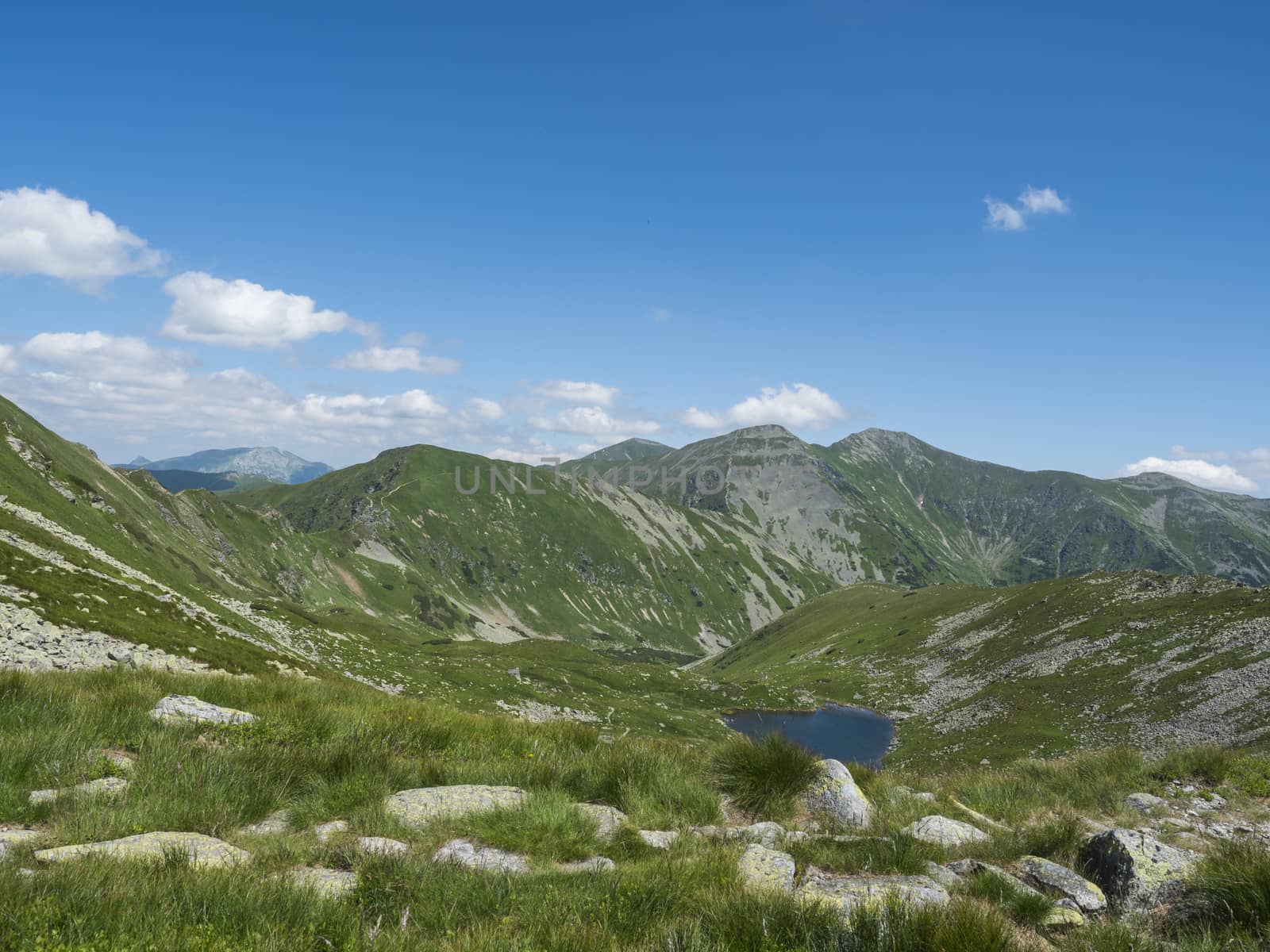 Beautiful vivid blue mountain lake Horne Jamnicke pleso with green mountain peaks view from the Jamnice sedlo saddle, Western Tatras mountains, Rohace, Slovakia, summer sunny day blue sky