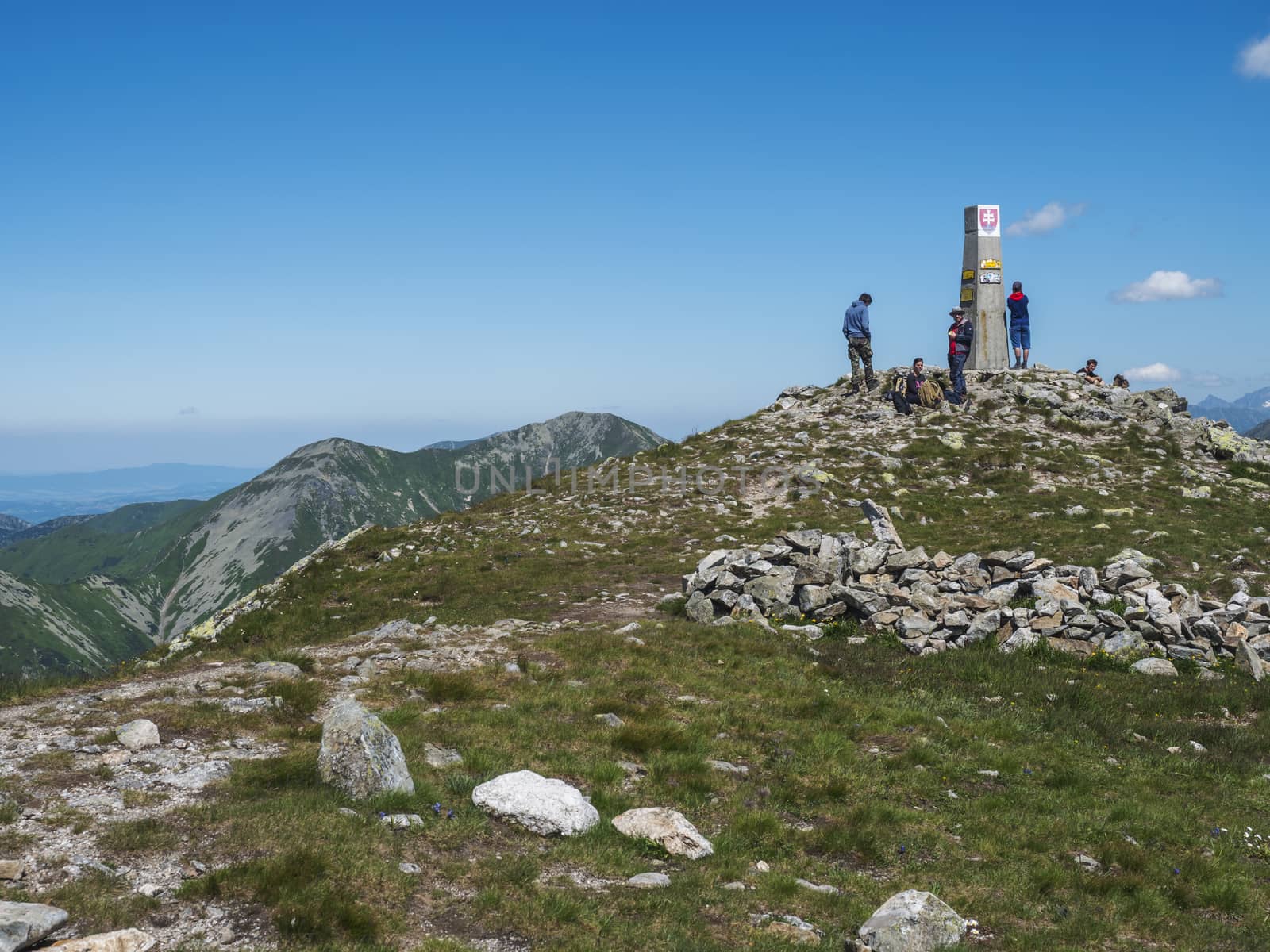 Slovakia, Western Tatra mountain, July 4, 2019: group of hiker people resting on top of Baranec peak in Western Tatra mountains with Rohace panorama. Sharp green mountains with hiking trail on ridge. Summer blue sky background.
