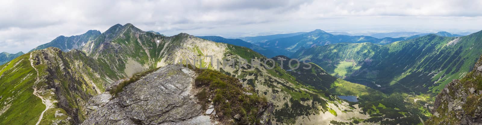 Panoramic view from Placlive peak on Western Tatra mountains or Rohace panorama. Sharp green mountains and lake rohacske pleso, ostry rohac, hruba kopa and volovec with hiking trail on ridge. Summer blue sky white clouds