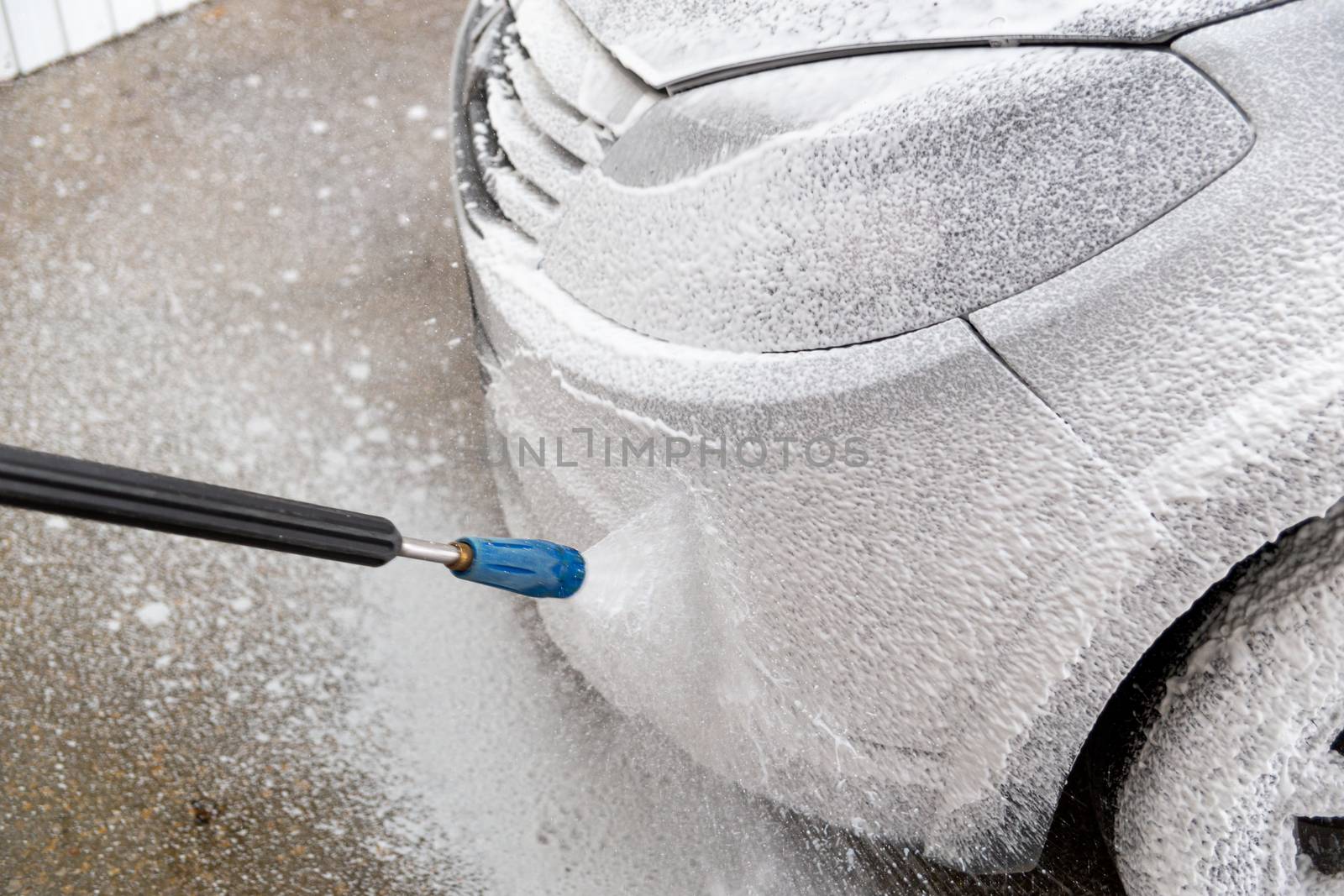 A closeup view of process of indoor wet car washing. Front side with headlamp. Applying soap sud.