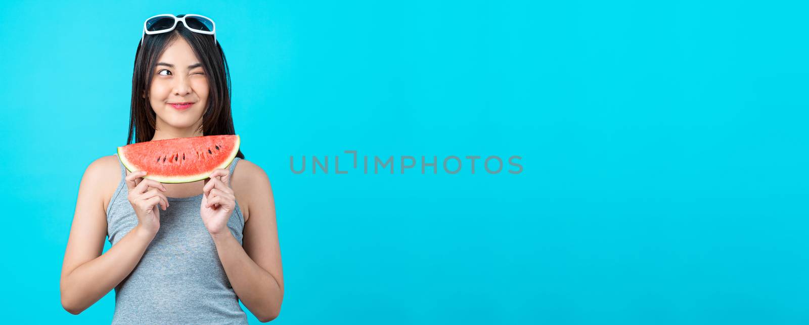 Banner of Asian young woman wearing summer vest and holding the Piece slide of watermelon on isolated blue color background, Sexy mouth bite, copy space and studio, fashion travel and tourist concept
