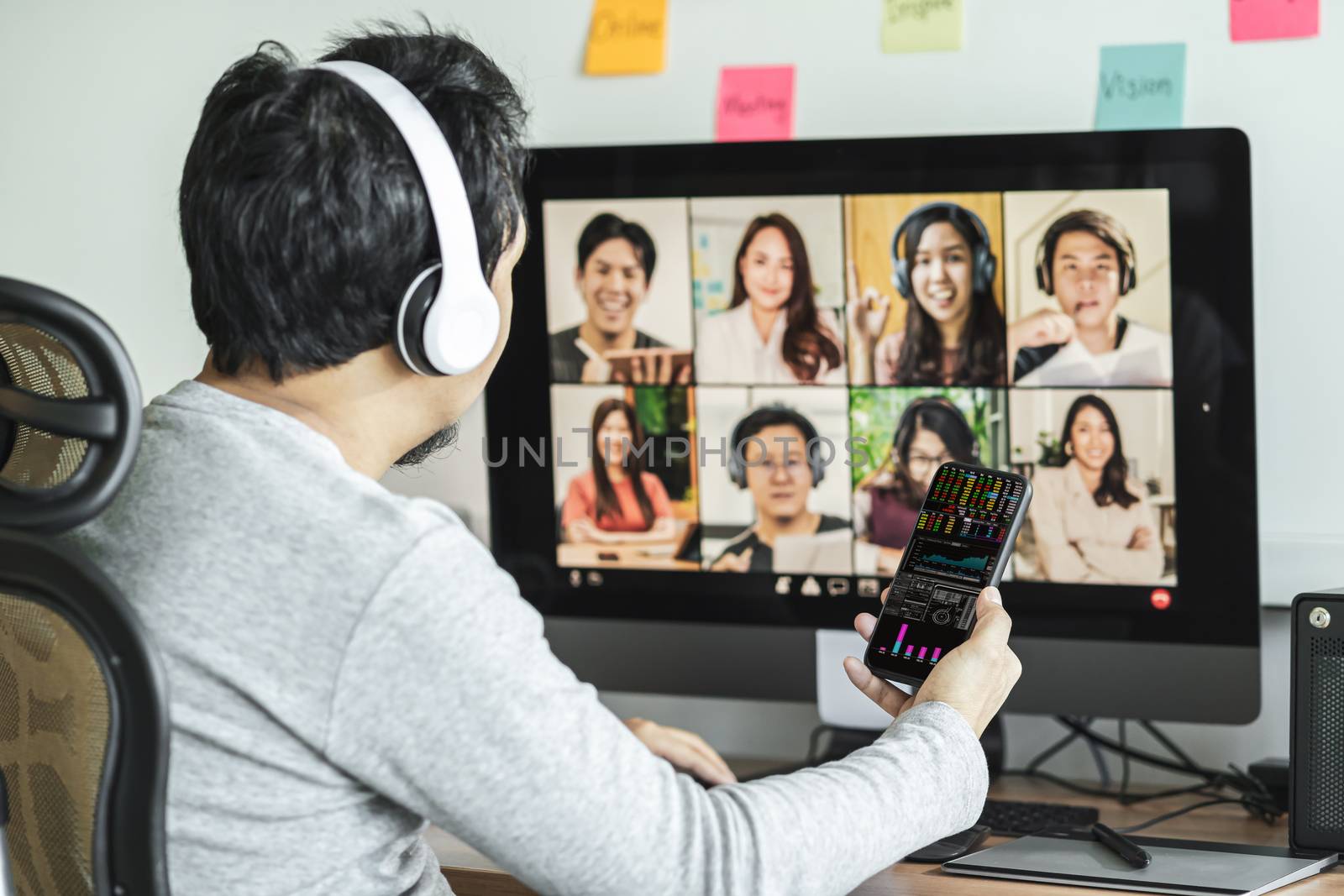 Rear view of Asian man using mobile phone and showing trading graph for working and online meeting via video conference with colleague when Covid-19 pandemic,education and Social distancing,new normal