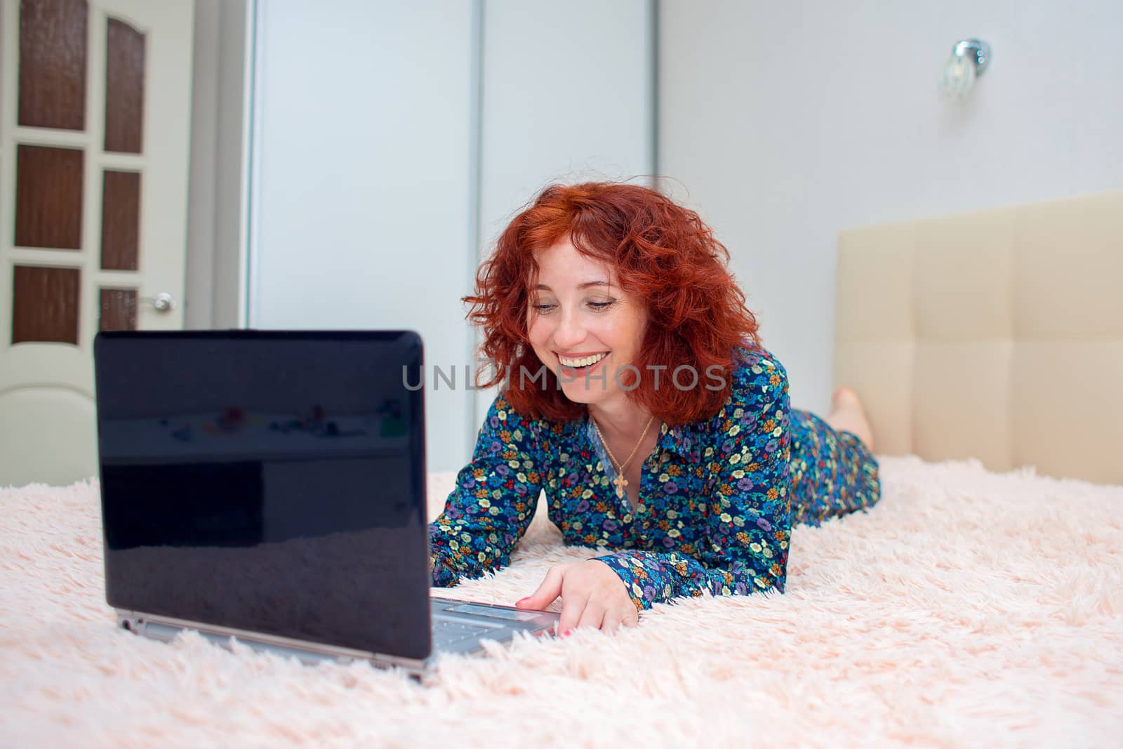 Curly bright woman working on the computer remotely lying on the bed
