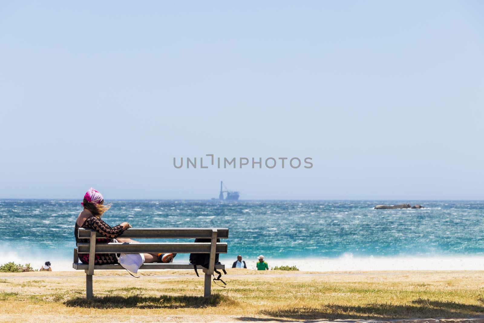 Woman on bench on the extremely windy beach, Camps Bay. by Arkadij