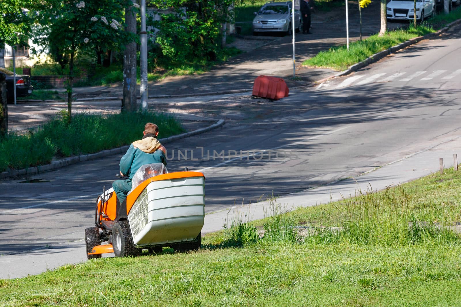 A utility worker takes care of roadside lawns, mowing tall grass with a professional lawnmower, image with copy space.