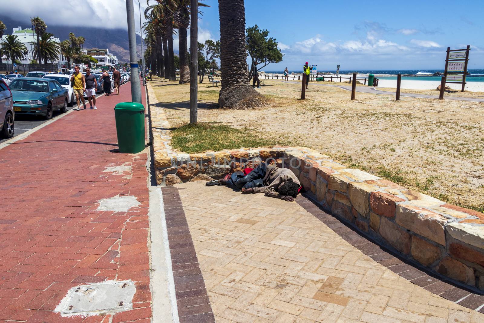 Poor homeless man sleeps on the street in the heat in Camps Bay, Cape Town, South Africa.