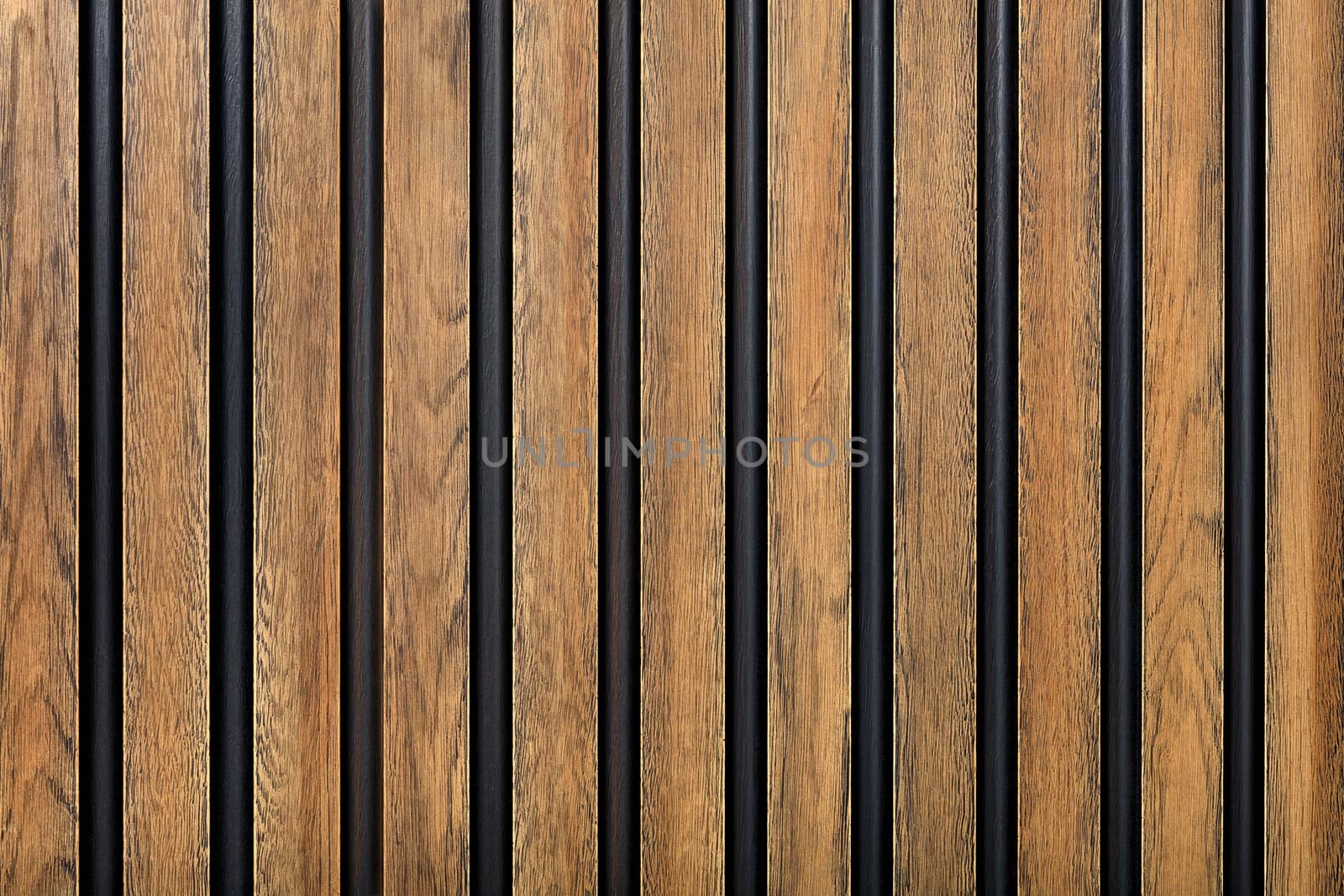 A wooden fence made of vertical decorative planks with a pronounced texture of light brown color with black spaces.