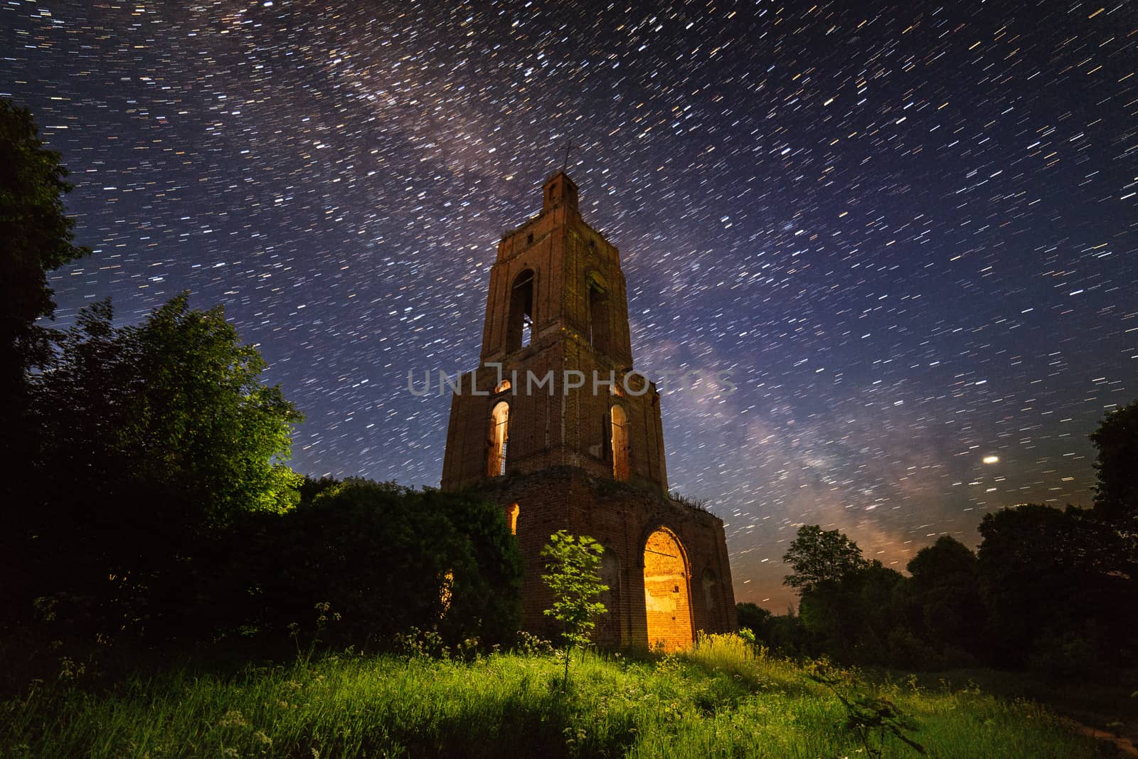 night brick bell tower ruin in forest at starry night with mystical internal light.