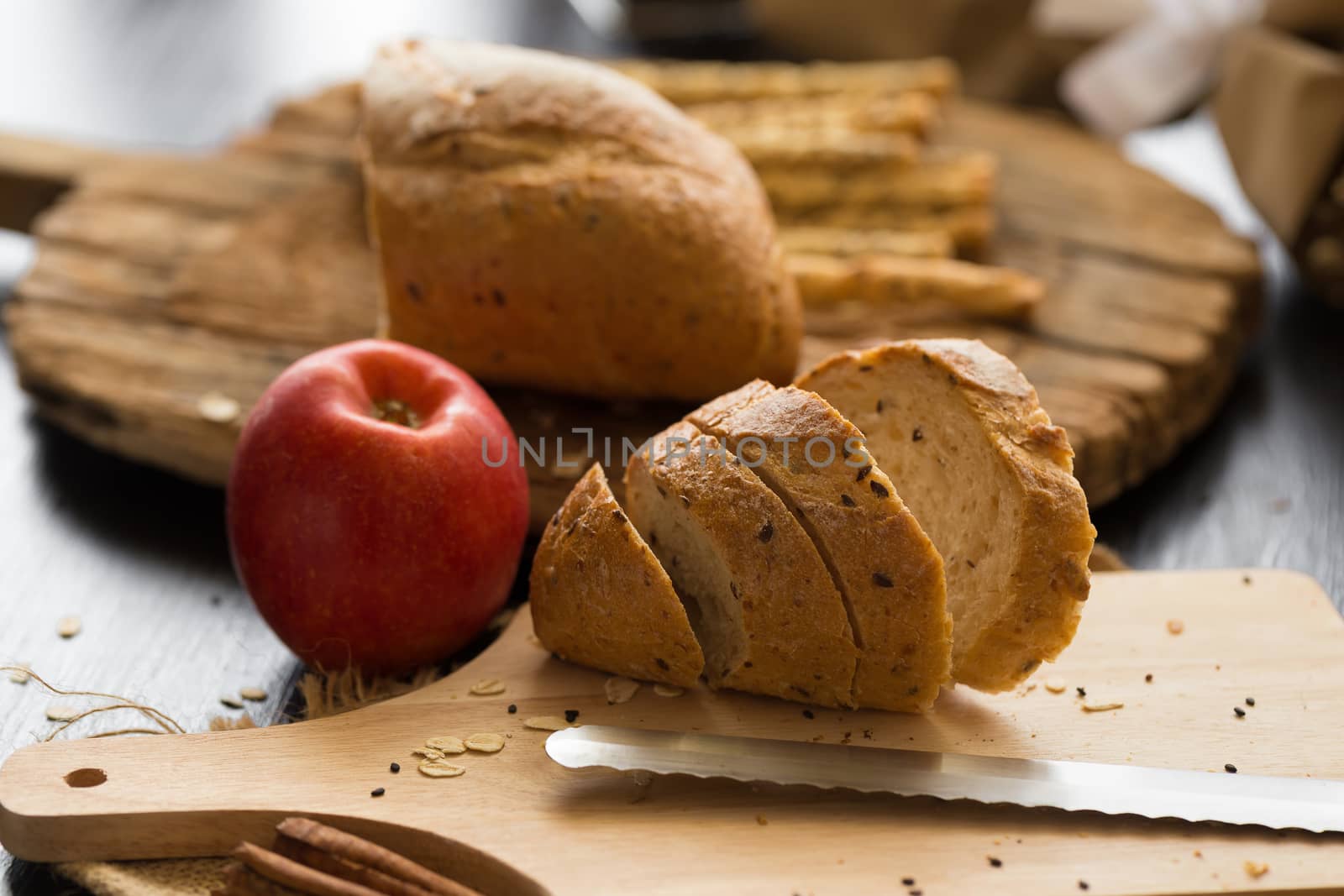 French bread baguette cut on wooden board with knife. with a chocolate butter and red apple.