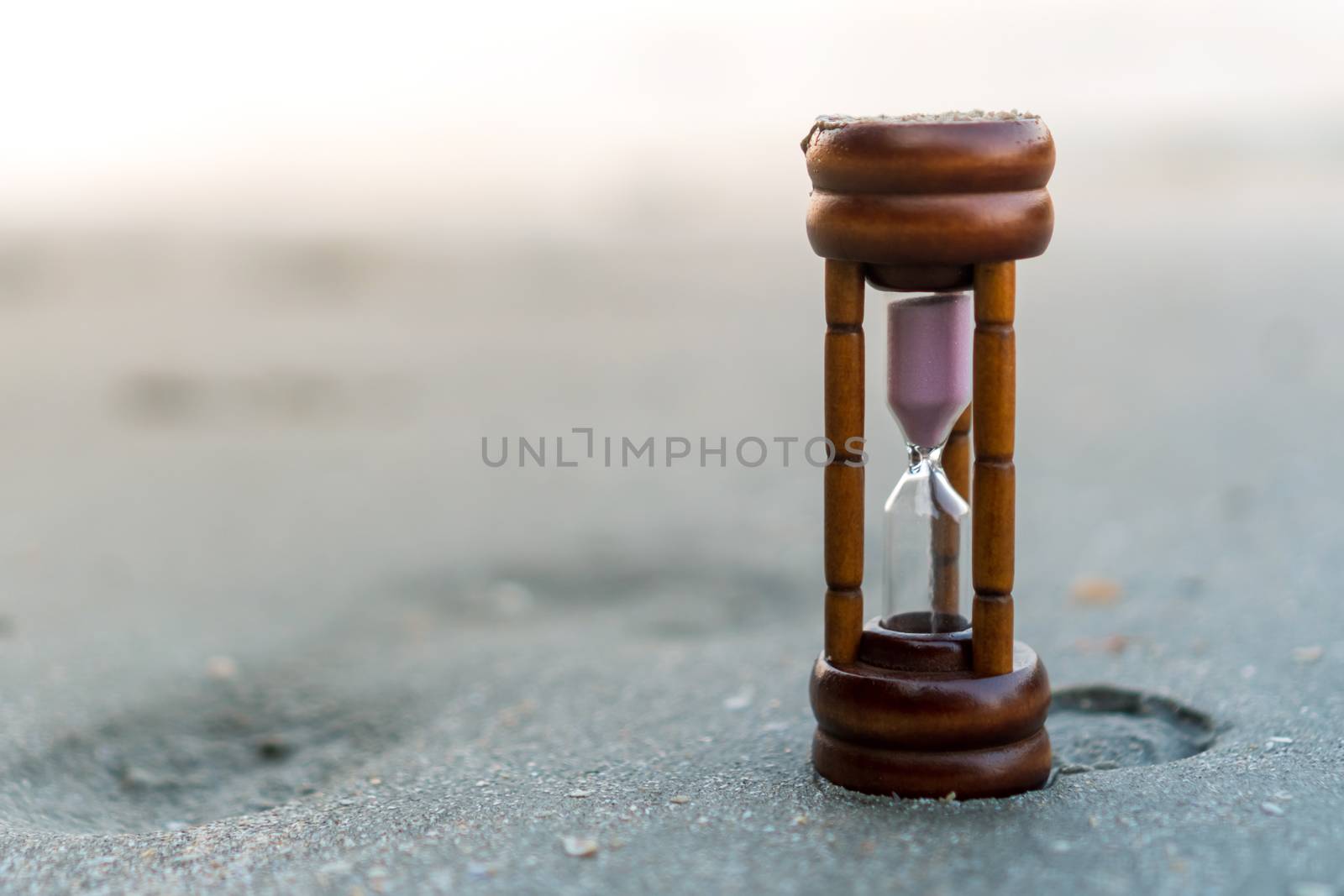 Small hourglass show time is flowing on sand beach background. by Suwant