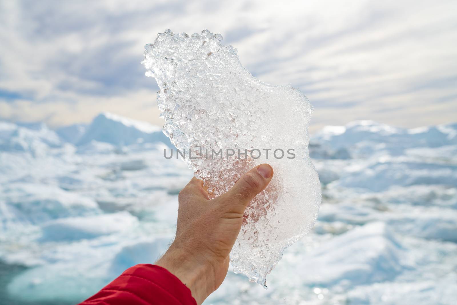 Global warming, climate change and Environmental protection concept with icebergs on Greenland. Hand holding melting ice by giant iceberg in Ilulissat icefjord on Greenland. Save the climate by Maridav