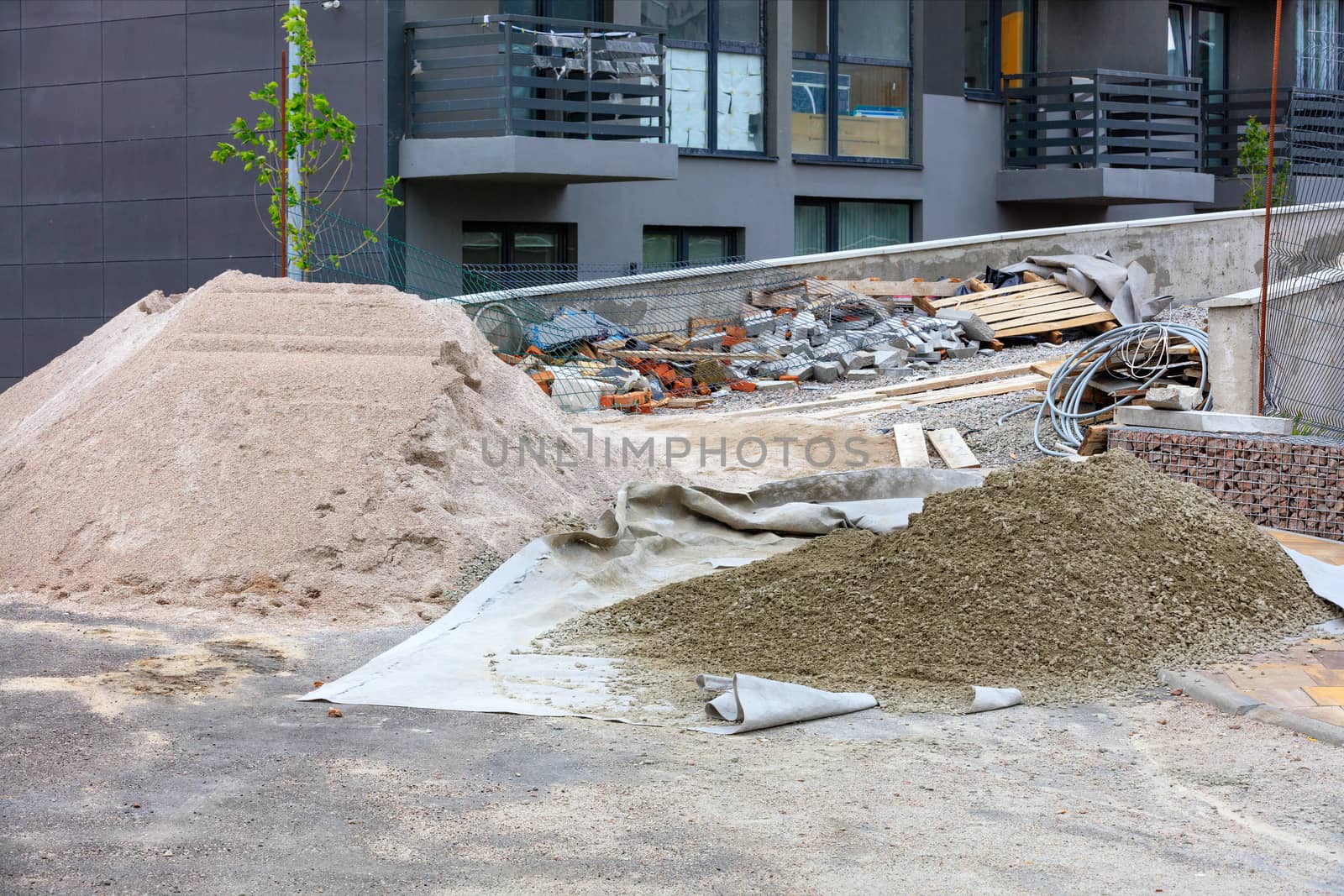 A workplace at a construction site with a pile of sifted sand and cement for laying paving slabs in the background of a new residential building under construction in blur.