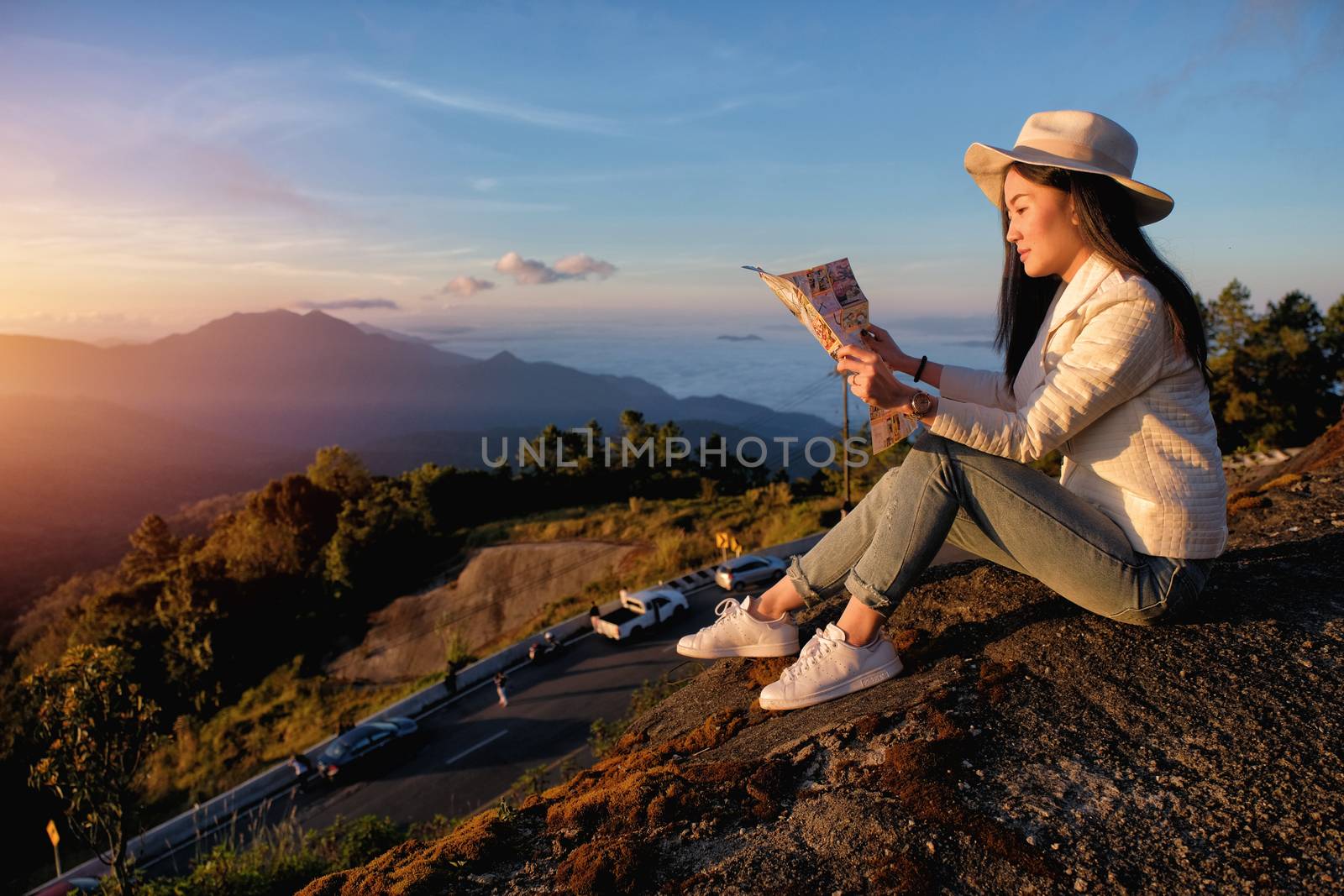 Happy woman reading a map siting on green grass meadow on top of by Surasak