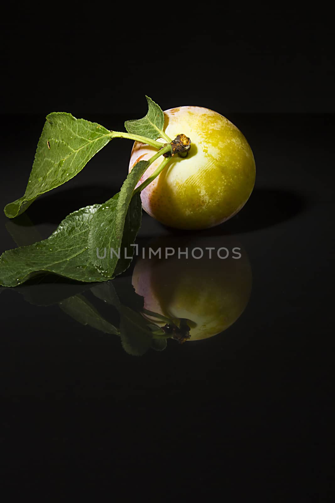 Ripe plums on a black reflective surface