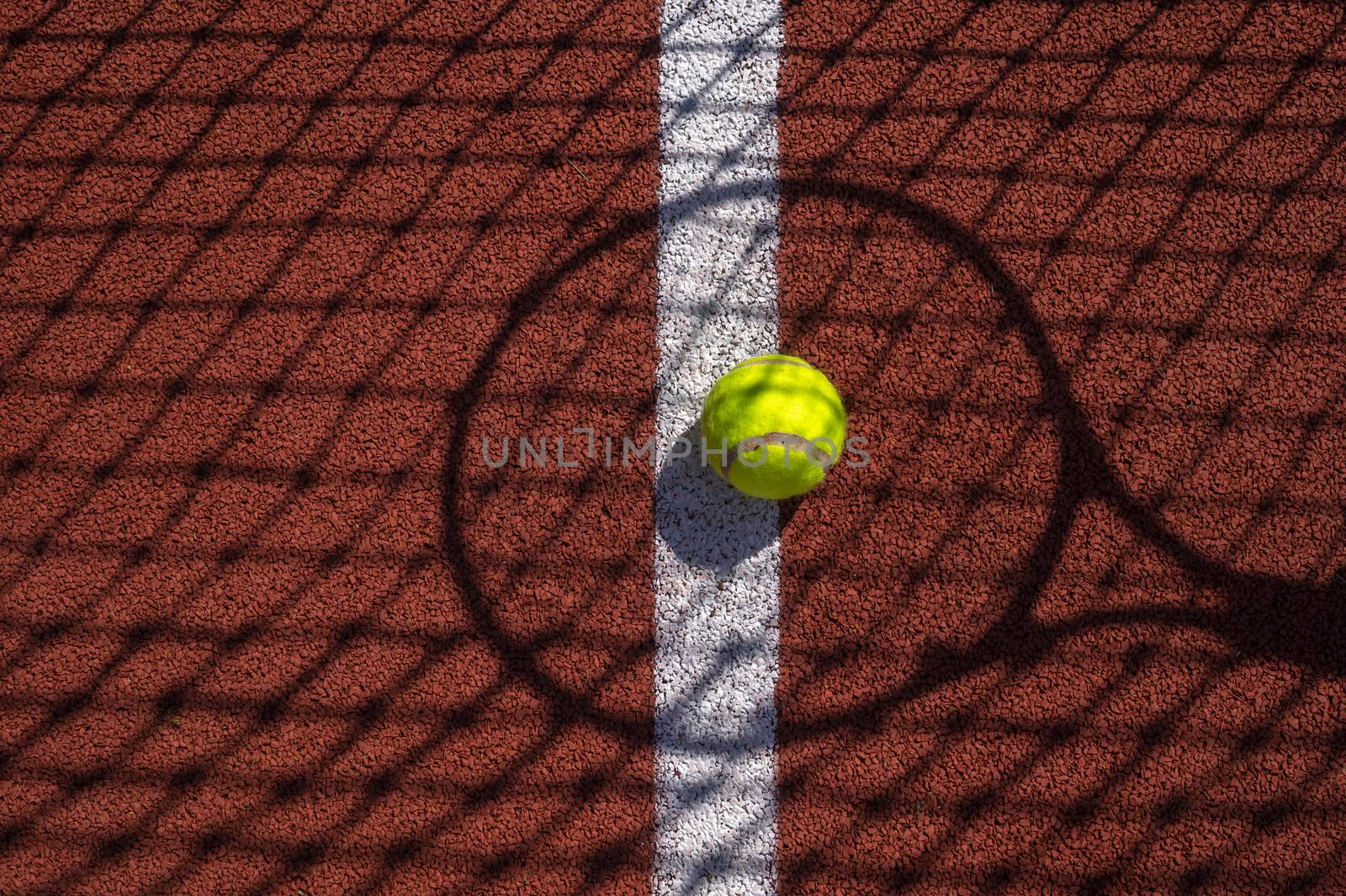 Shadows of net and racket surrounding a tennis ball on a white line on an outdoor court in sunshine in a sport and active lifestyle concept