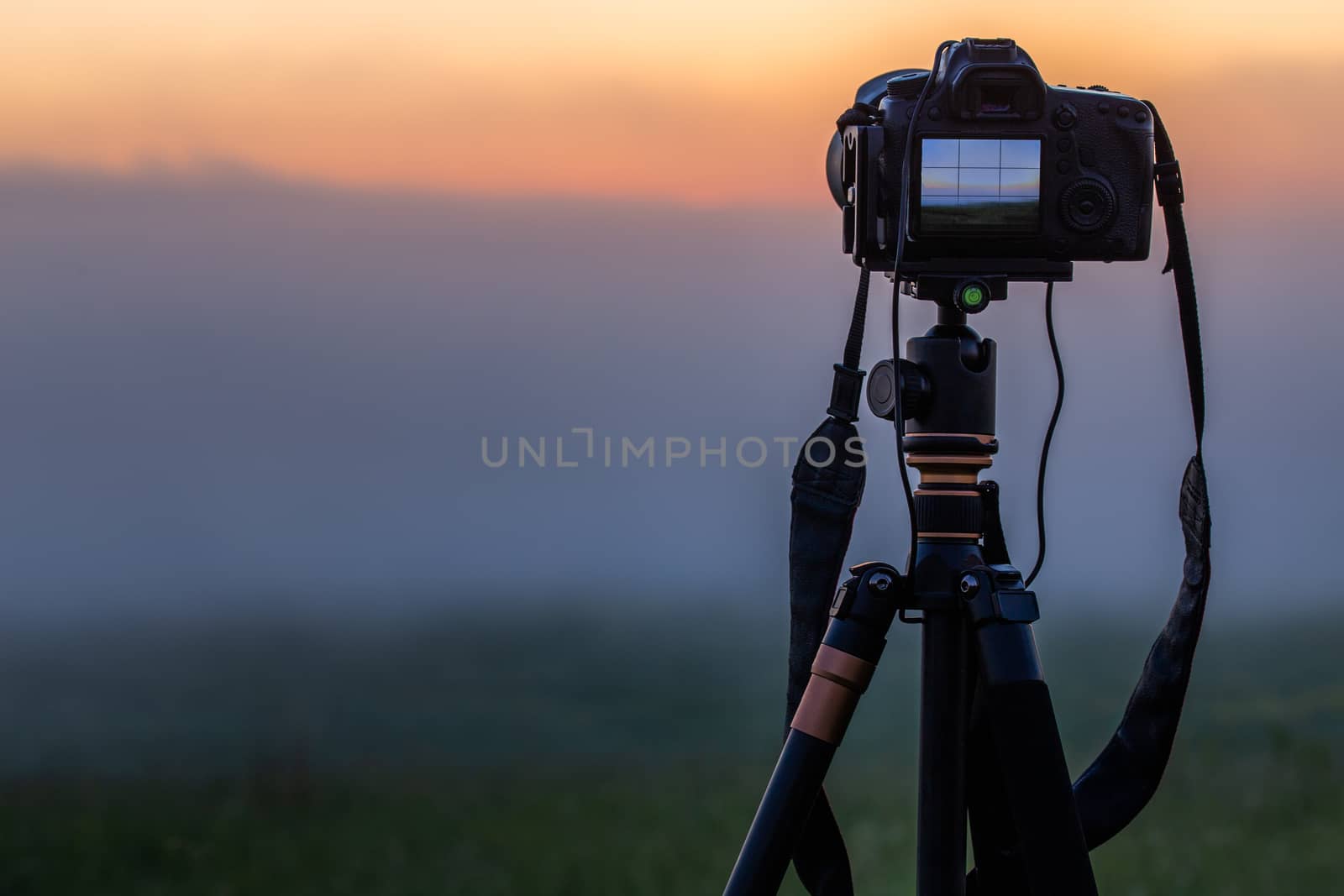 black digital camera on tripod shooting foggy morning landscape at summer with selective focus.