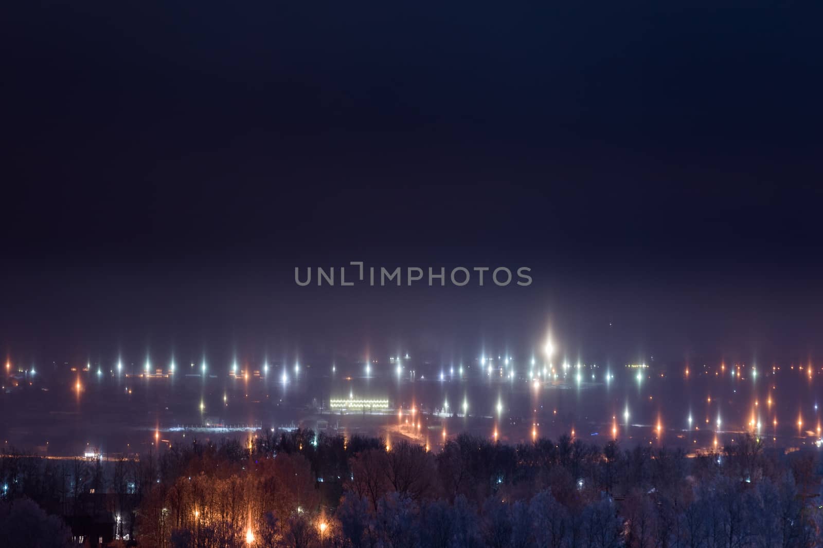 night winter cityscape with light pillars atmospheric phenomenon.