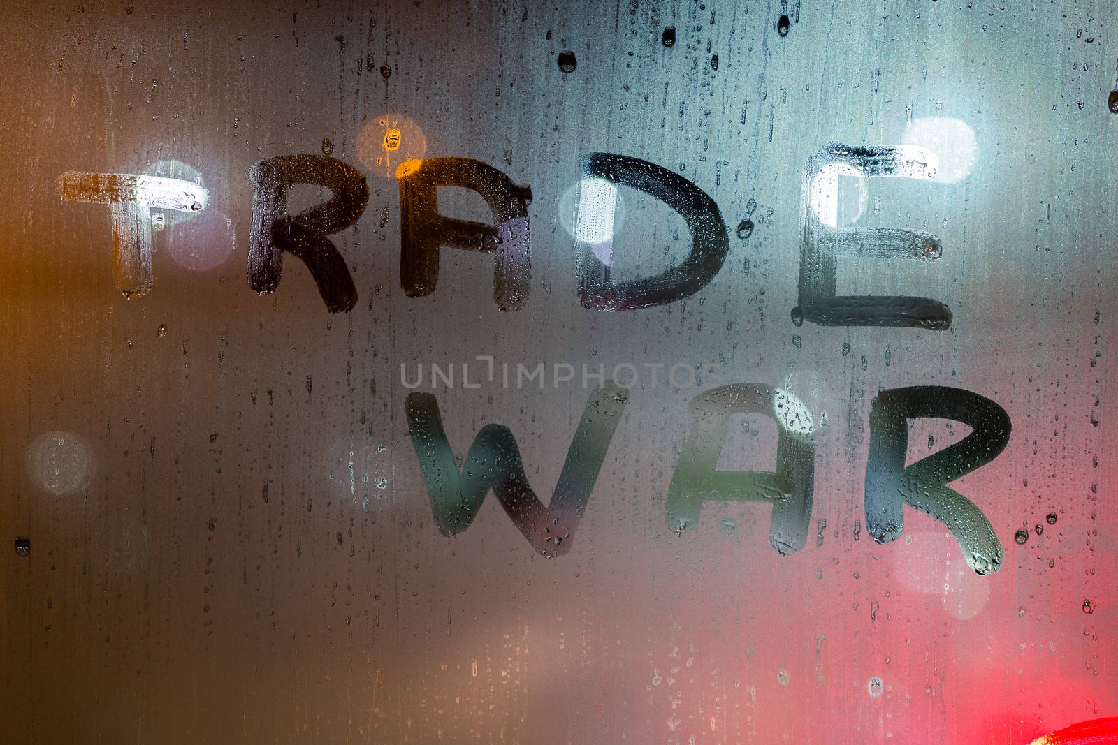 the words trade war written on night wet window glass close-up with blurred background.