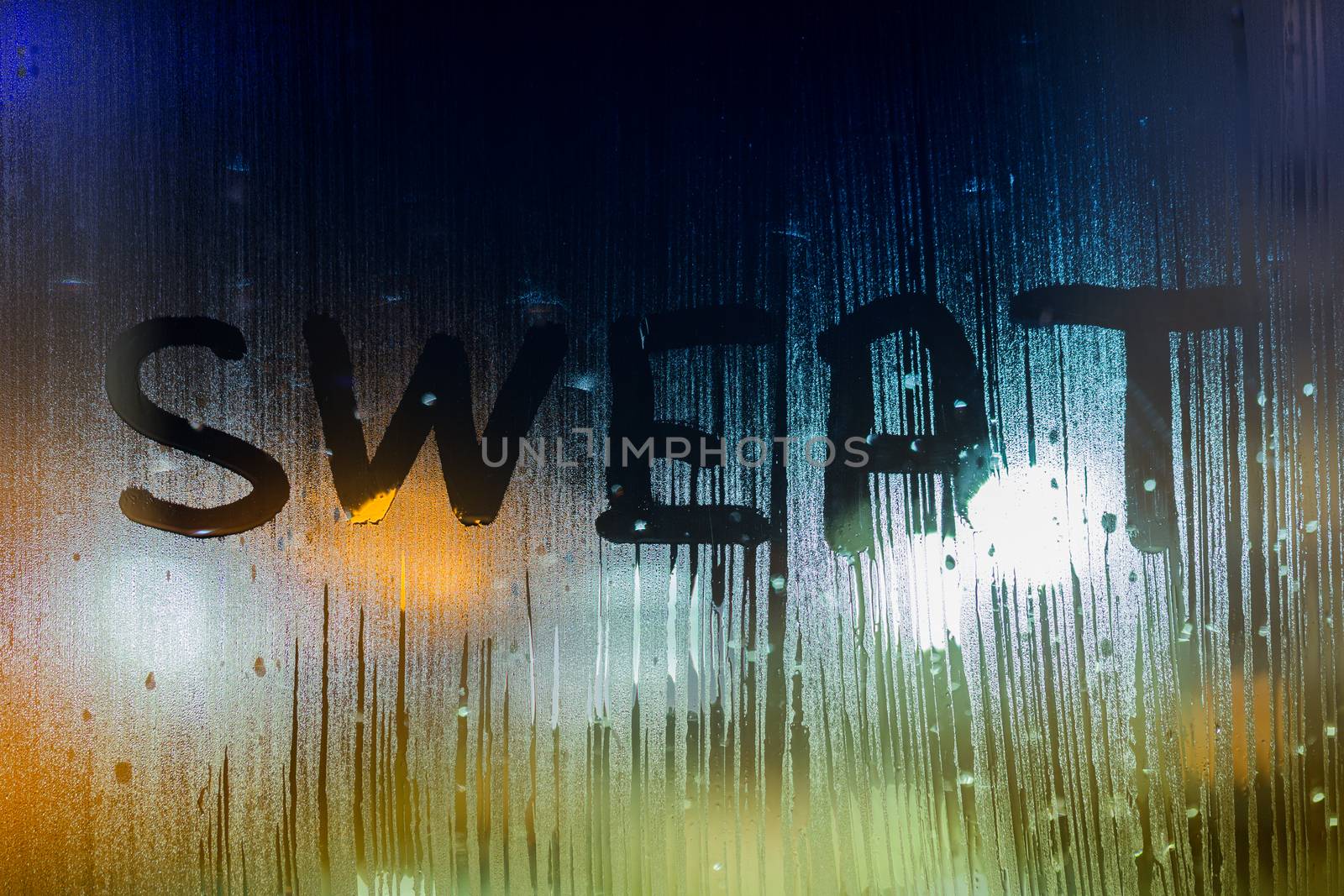 the word sweat written on night wet window glass close-up with bokeh background.