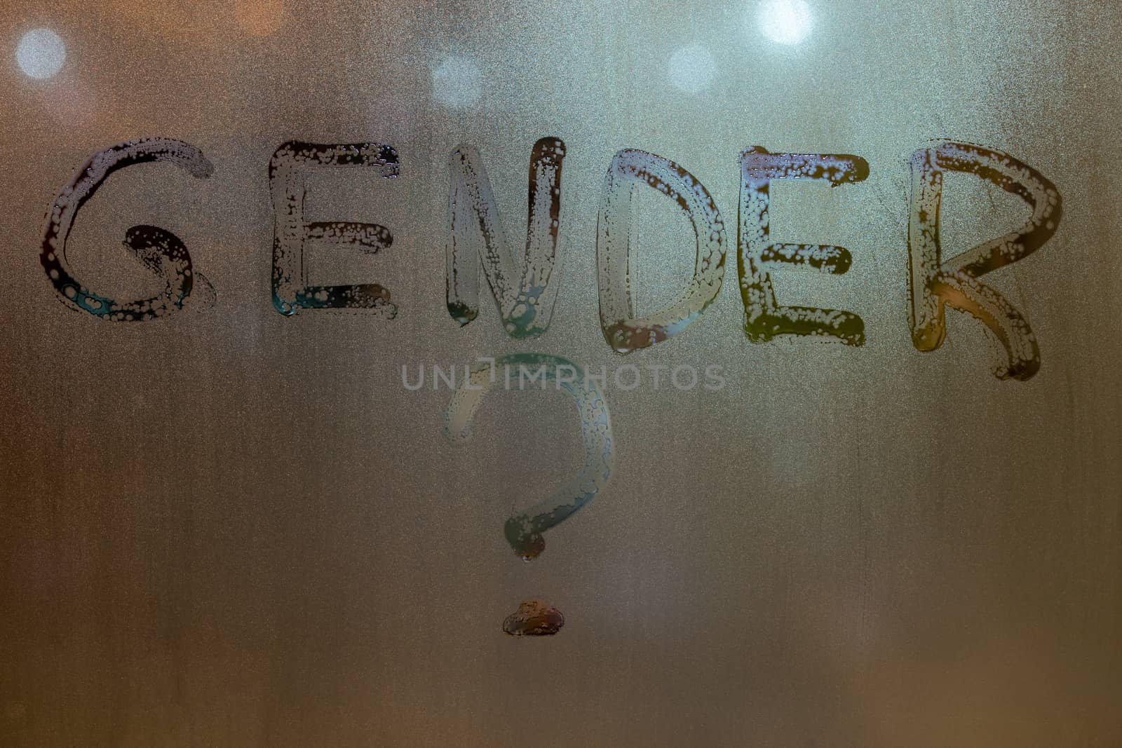 the question gender written by finger on night wet glass with blurred lights in background.
