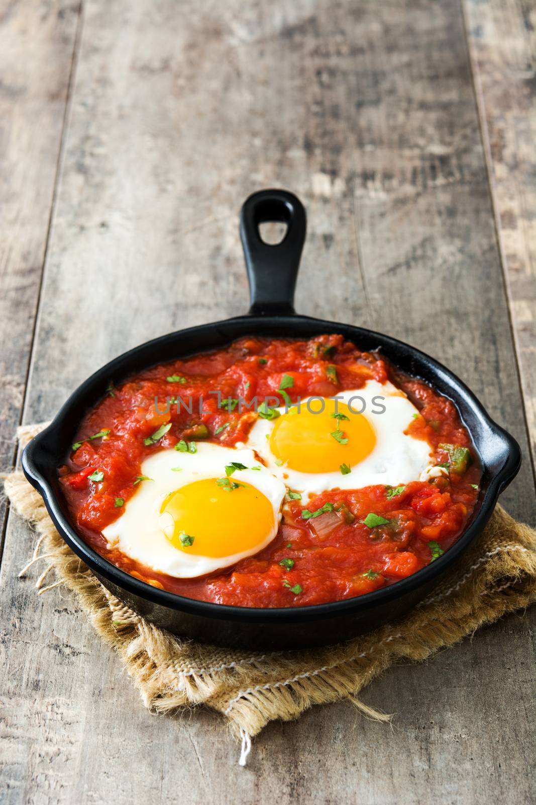 Mexican breakfast: Huevos rancheros in iron frying pan on wooden table by chandlervid85