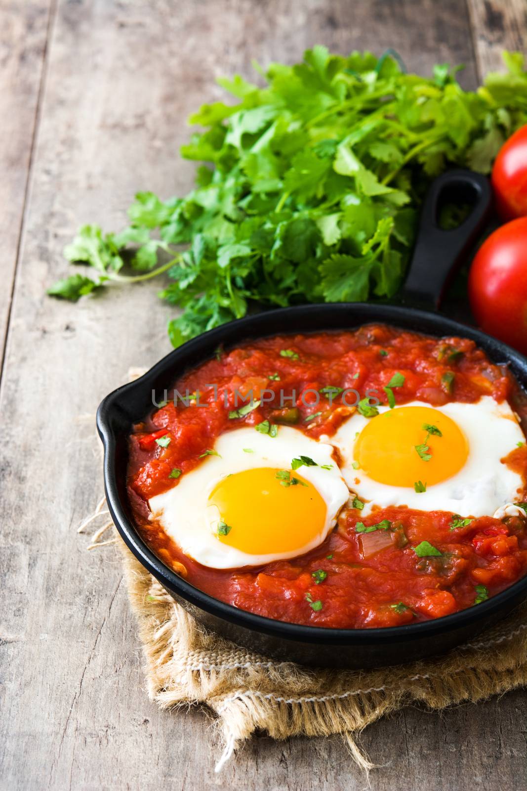 Mexican breakfast: Huevos rancheros in iron frying pan on wooden table by chandlervid85