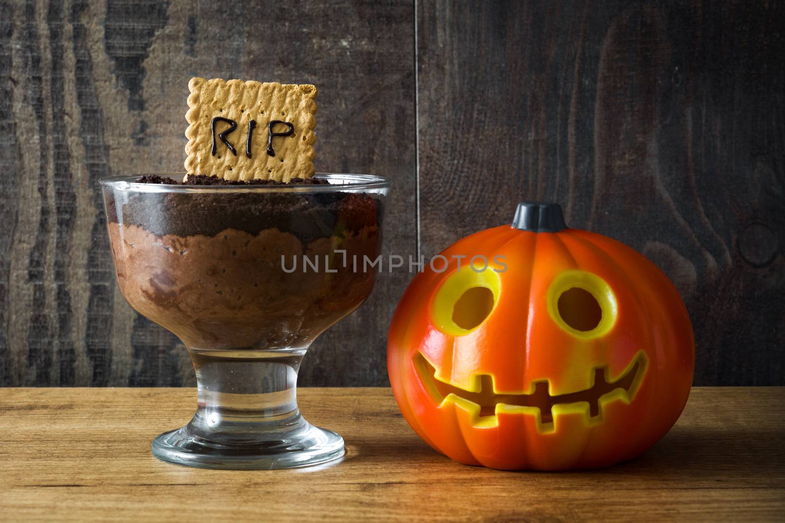 Funny Halloween chocolate mousse with tomb cookie on wooden table