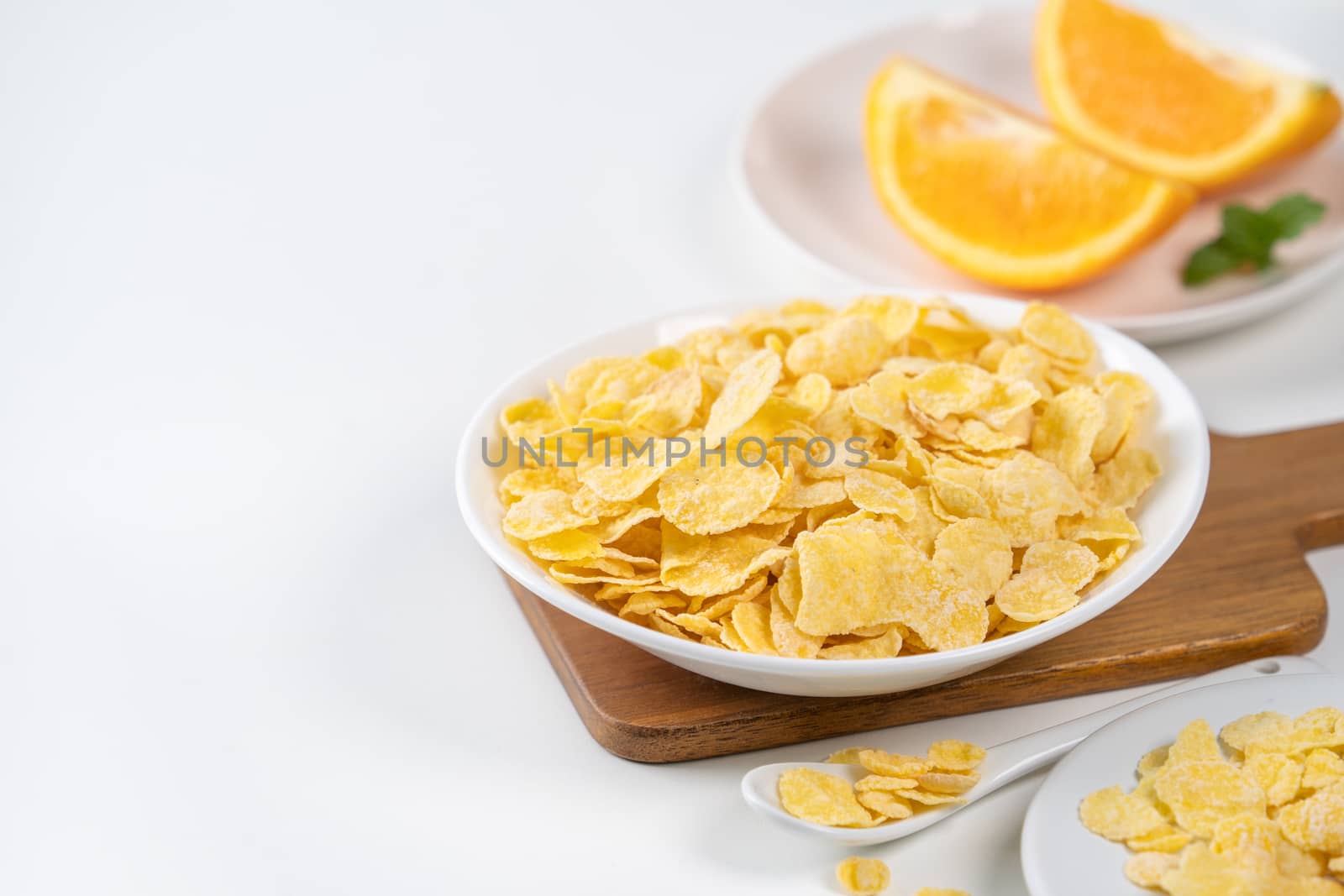 Corn flakes bowl sweeties with milk and orange on white background, close up, fresh and healthy breakfast design concept.