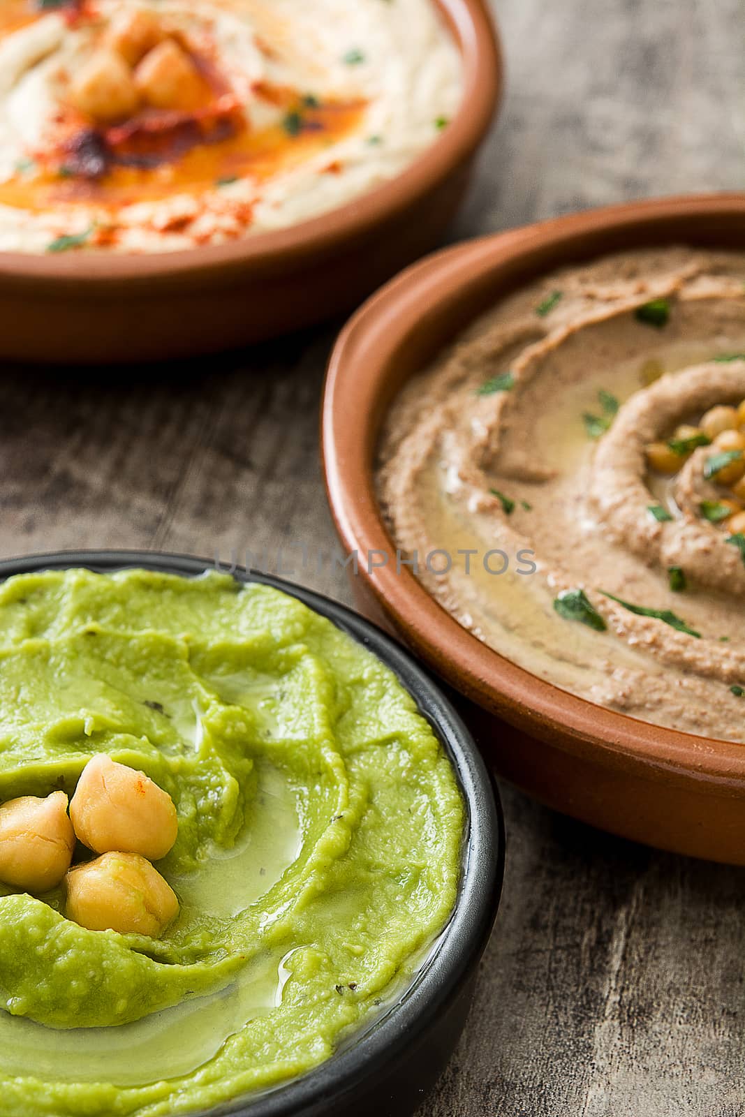Different hummus bowls. Chickpea hummus, avocado hummus and lentils hummus on wooden table by chandlervid85
