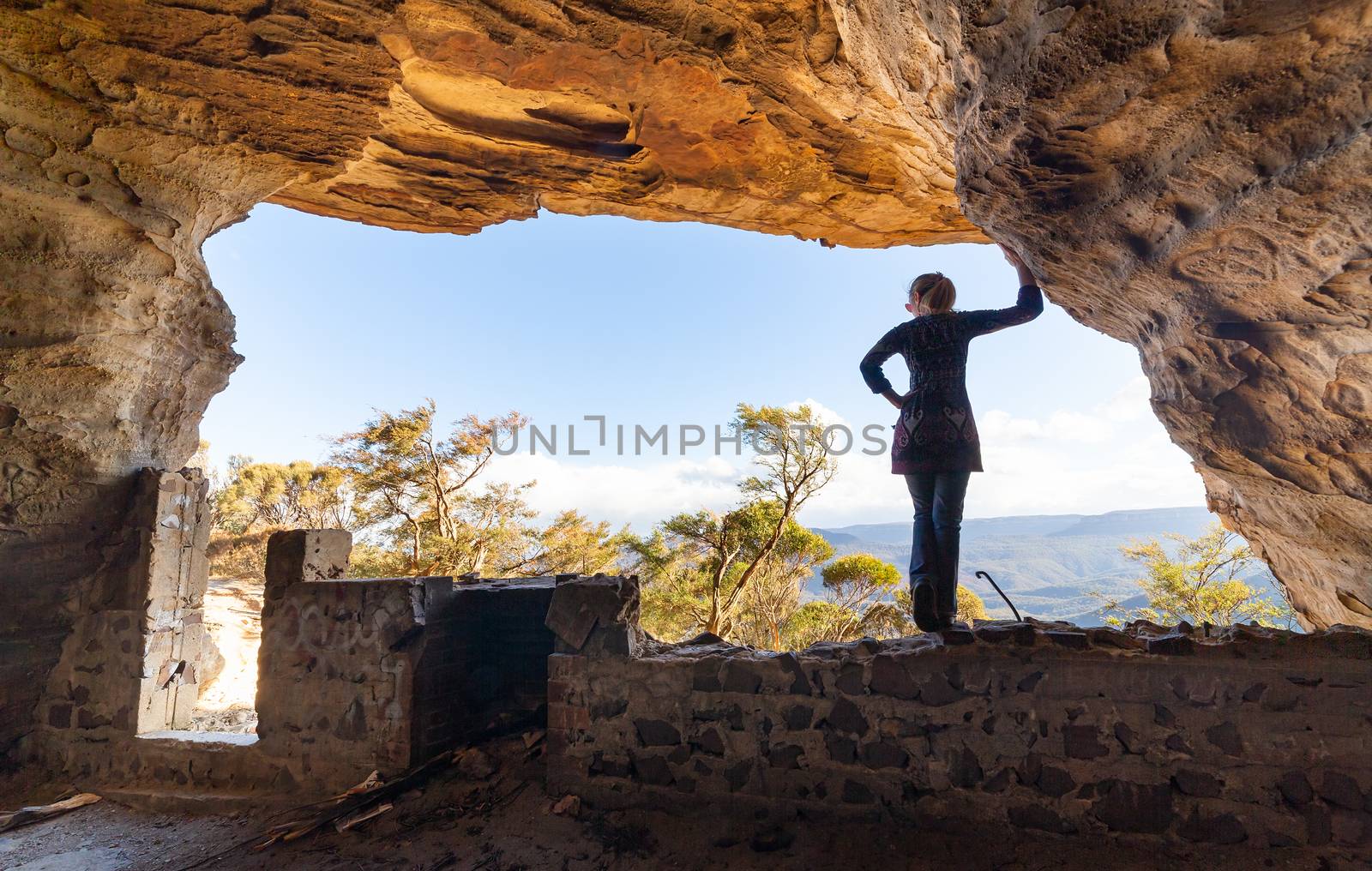 View from inside a cave of a woman looking out to mountain views overlooking Jamison Valley from a cave with a rustic fire pit