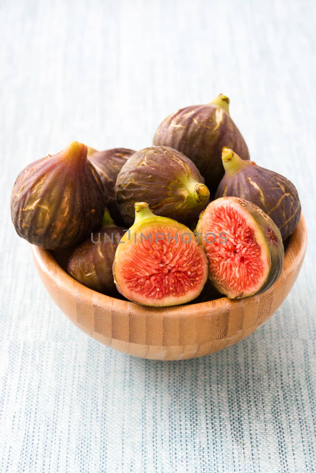 Fresh figs on wooden bowl and blue background by chandlervid85