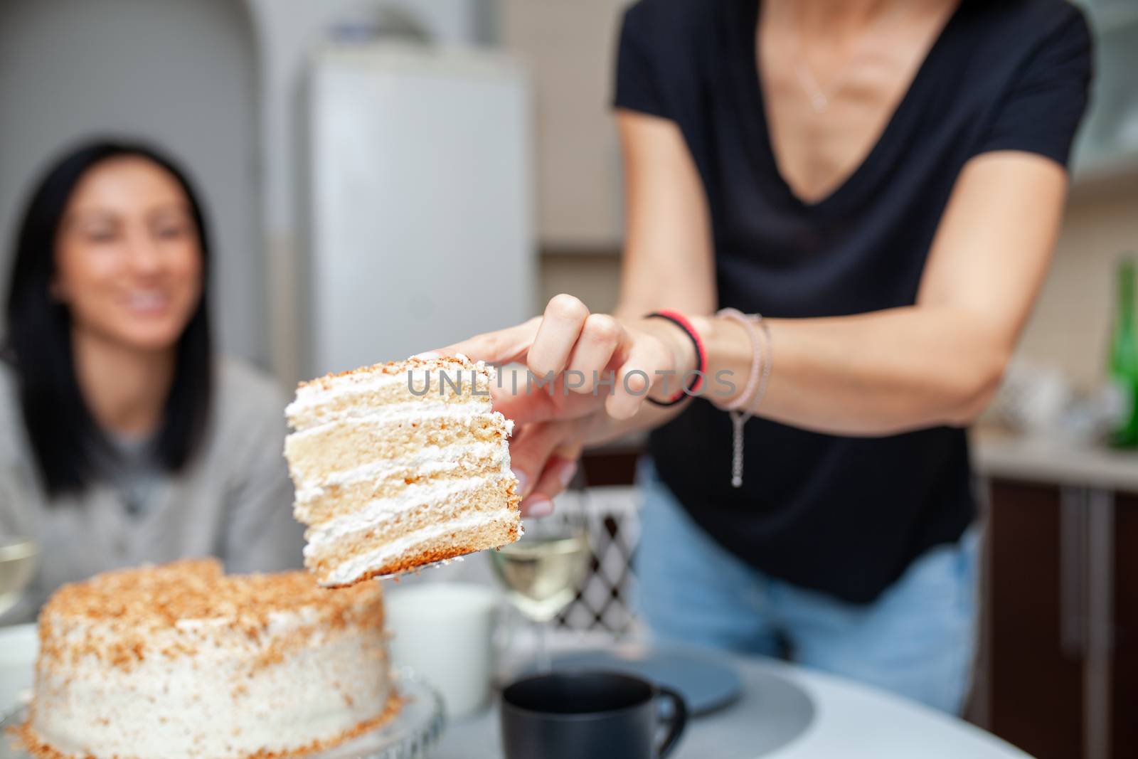 Friends meeting with wine and cake in the modern style kitchen. Women smile and joke. Two girls drink wine in the home kitchen.