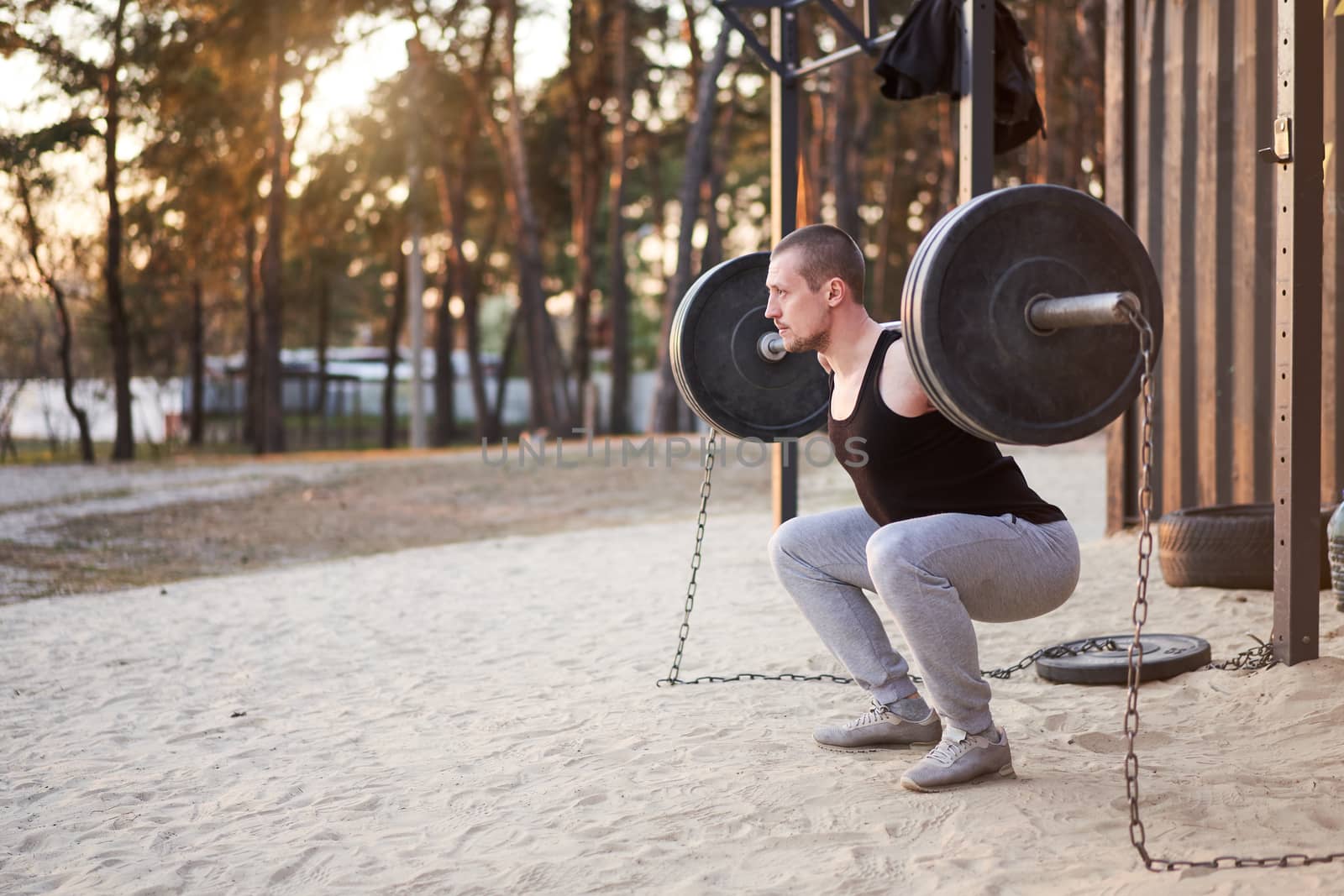 Man with barbell outdoor gym on nature in park. Young adult caucasian athlete lifts a barbell with a heavy weight does sports. Healthy lifestyle concept. Sport in quarantine. Copy space