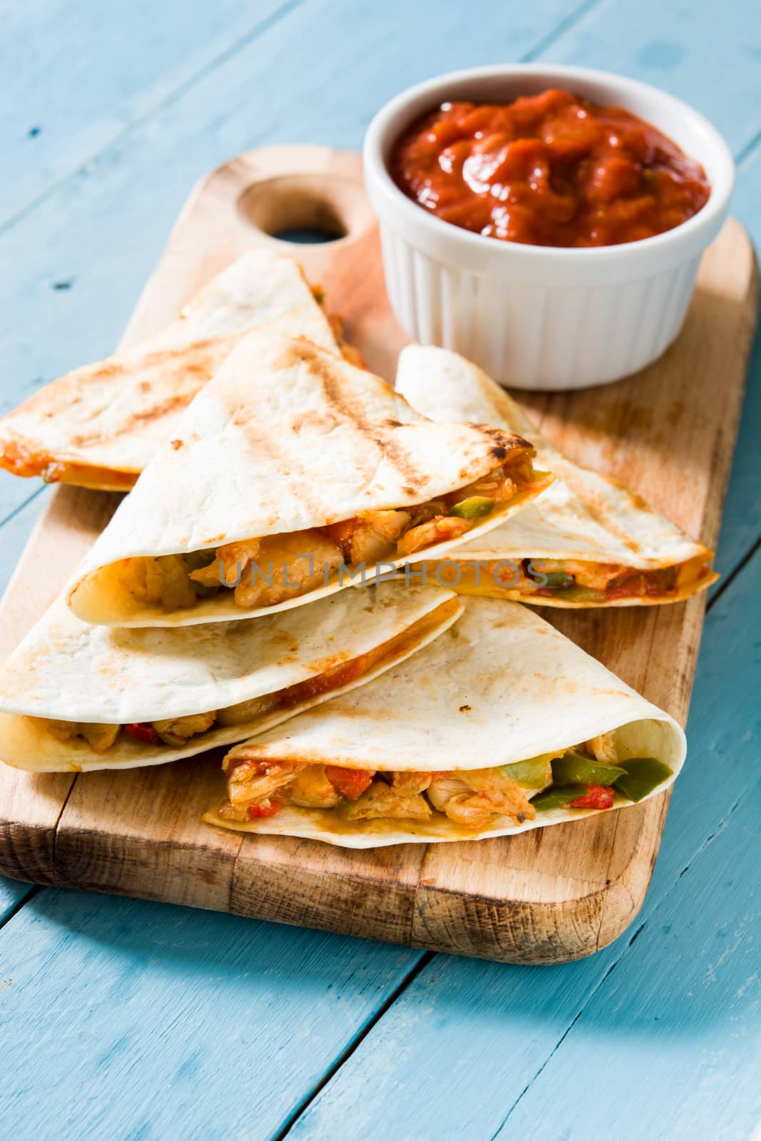 Mexican quesadilla with chicken, cheese and peppers on blue wooden table.