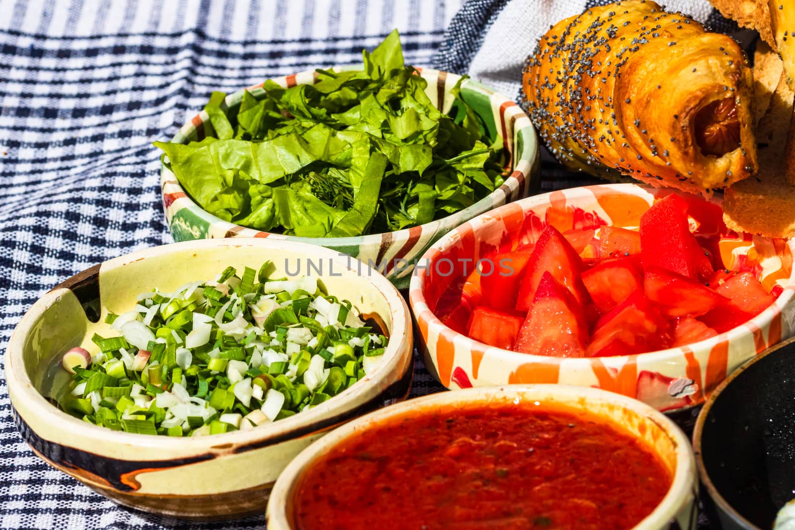 Rustic composition with sausages rolls and different bowls with sauce and chopped vegetables ( tomatoes, green lettuce, green onion, green garlic)