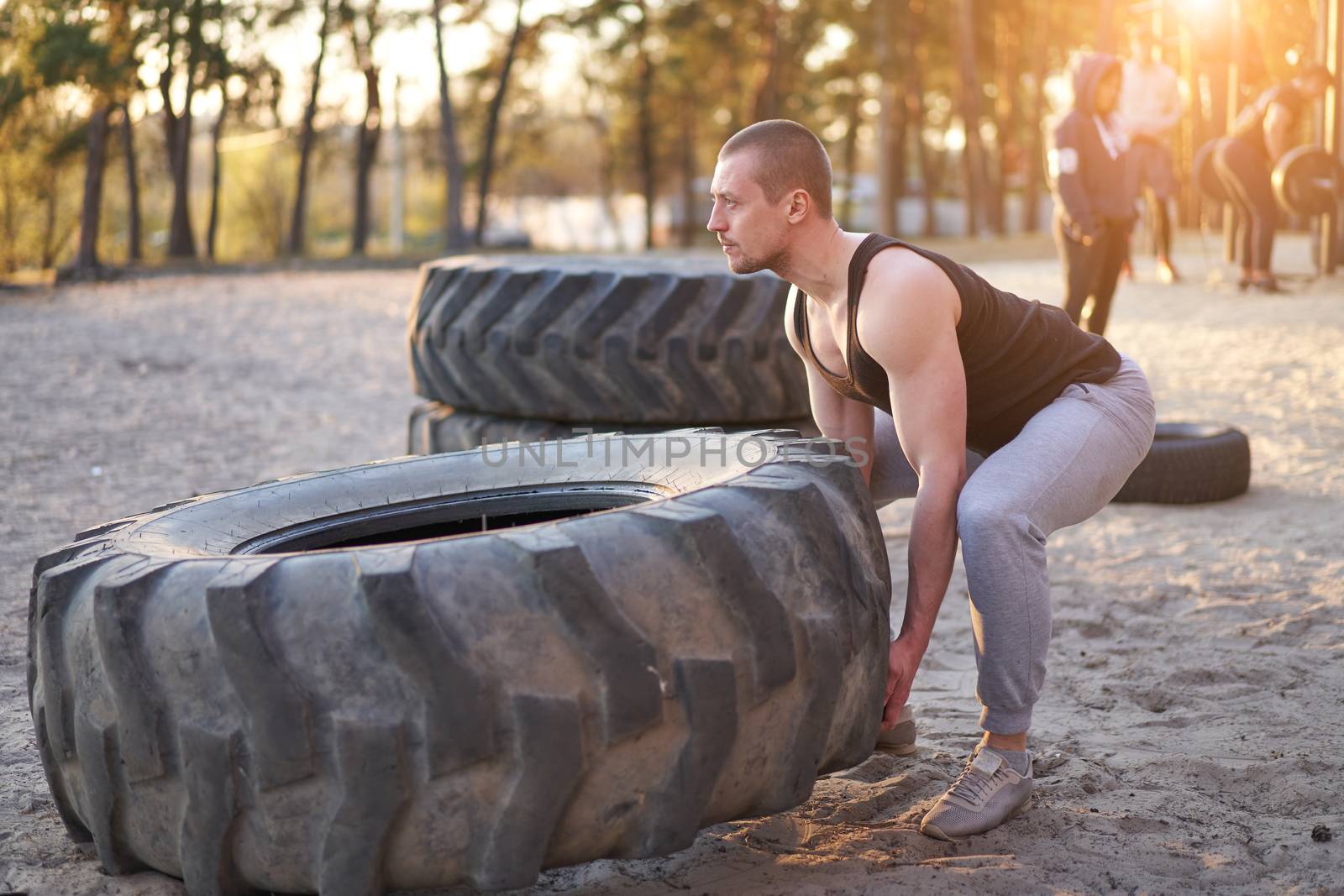 Strong man training workout lifting large tire outdoor DIY gym. Sportive young adult caucasian guy flip big wheel on nature. Handmade equipment sport exercising helthy lifestyle concept