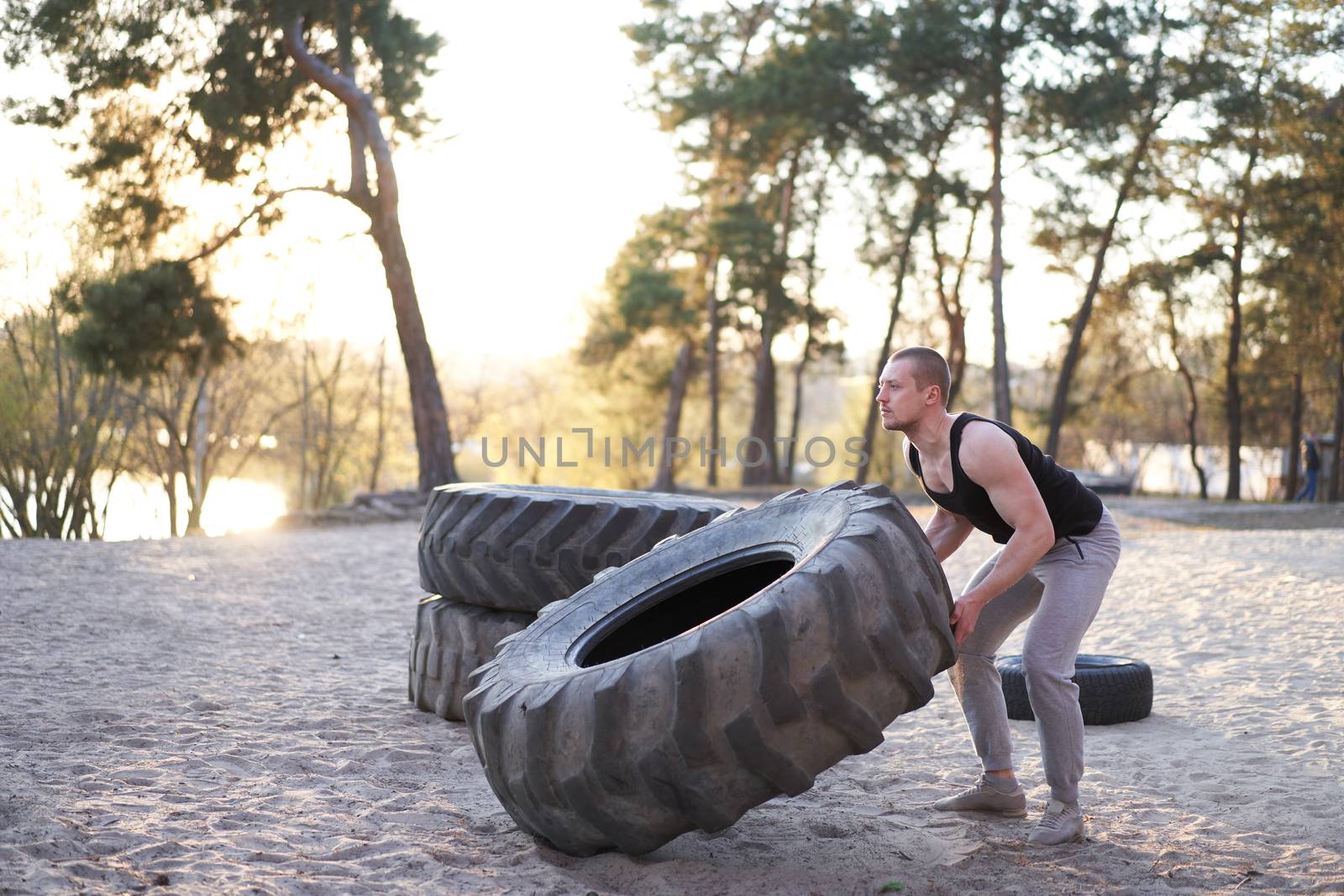Strong man training workout lifting large tire outdoor DIY gym. Sportive young adult caucasian guy flip big wheel on nature. Handmade equipment sport exercising helthy lifestyle concept
